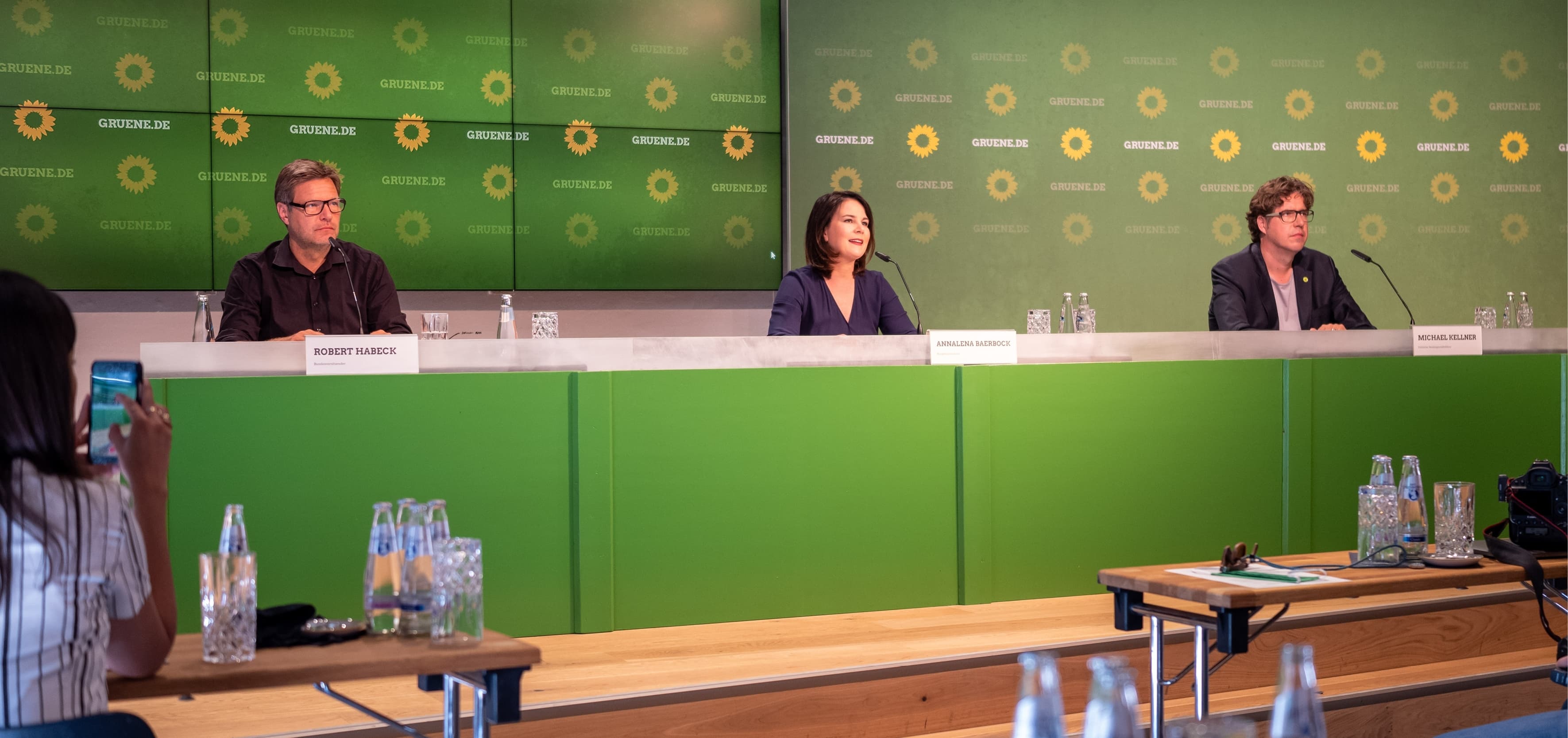 Robert Habeck, Annalena Baerbock und Michael Kellner sitzen vor einer grünen Wand bei einer Pressekonferenz.