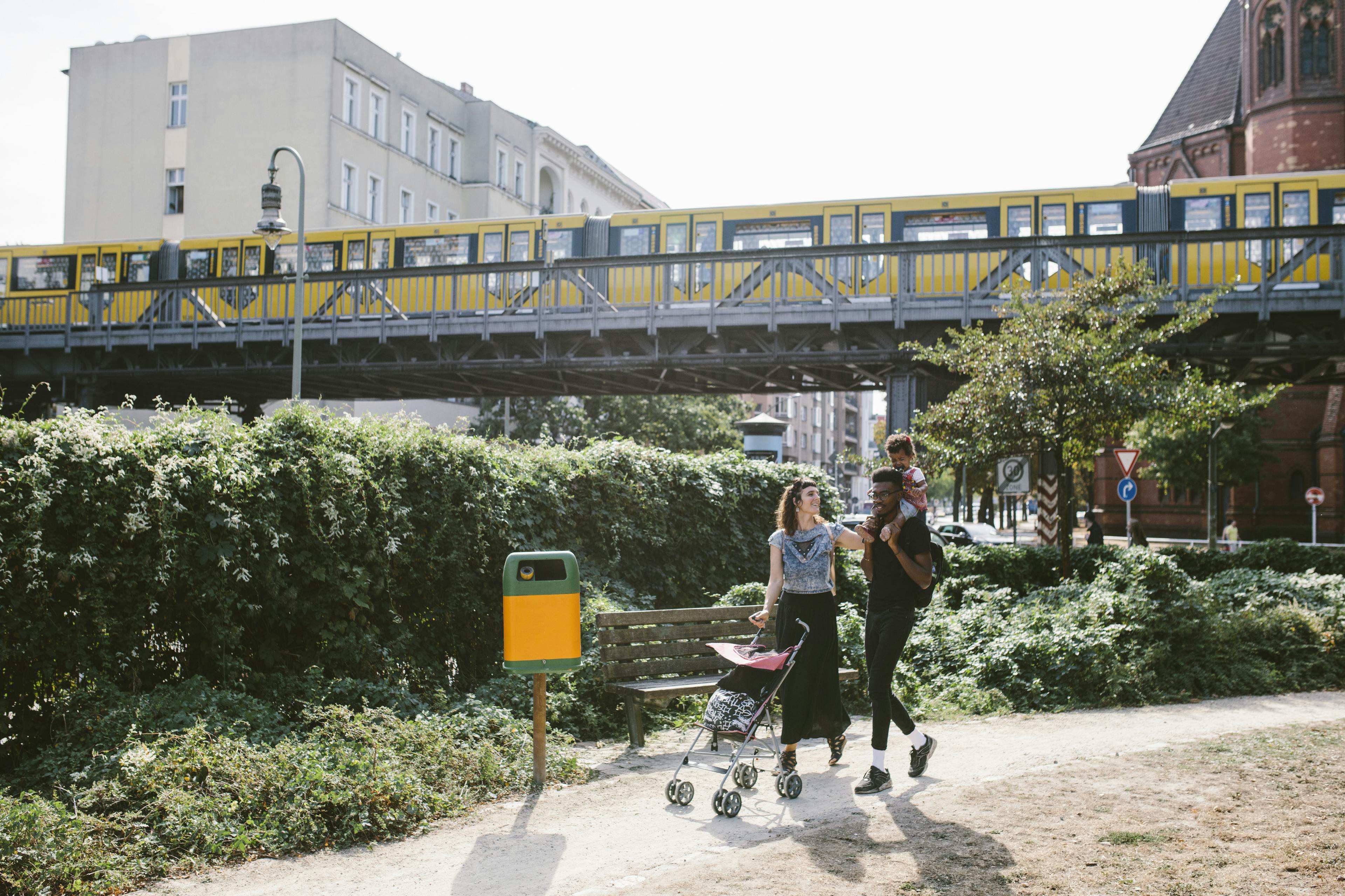 Eine dreiköpfige Familie in urbanem Umfeld spaziert im Park.