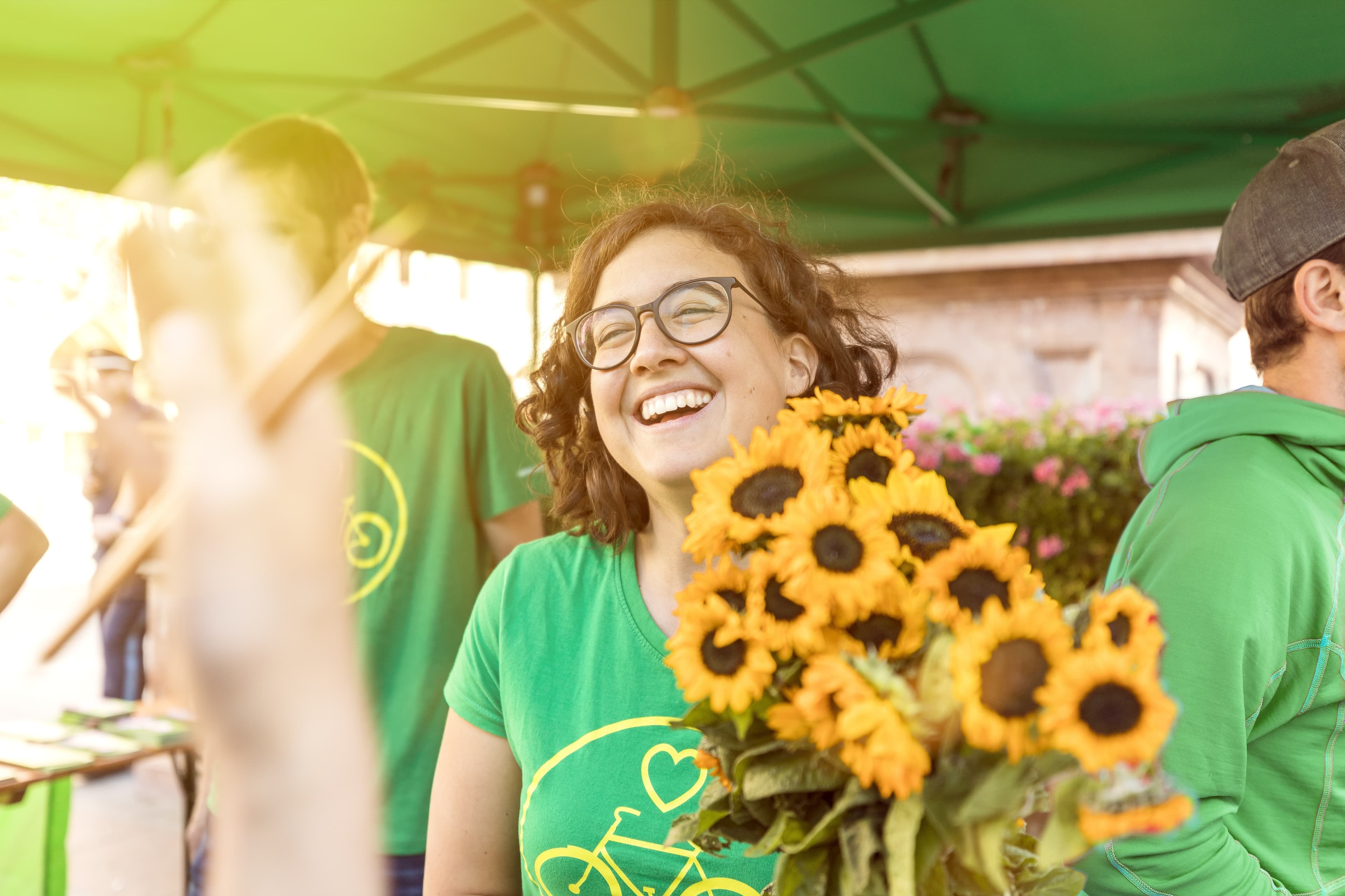 Frau mit grünem Shirt, auf dem gelbes Fahrrad abgebildet ist, hält einen Strauß Sonnenblumen.