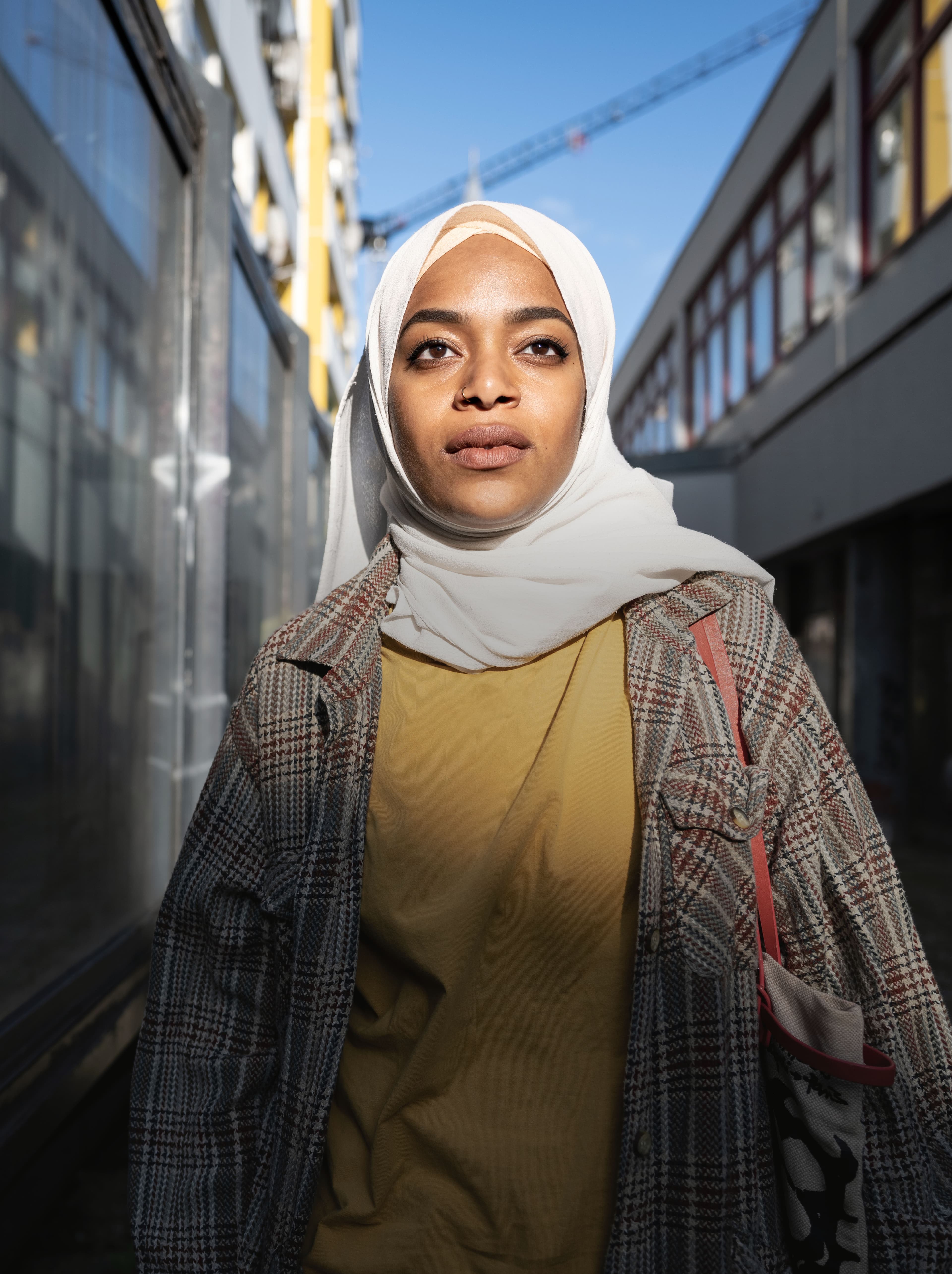 Eine Person of Colour mit Kopftuch zwischen Gebäuden.