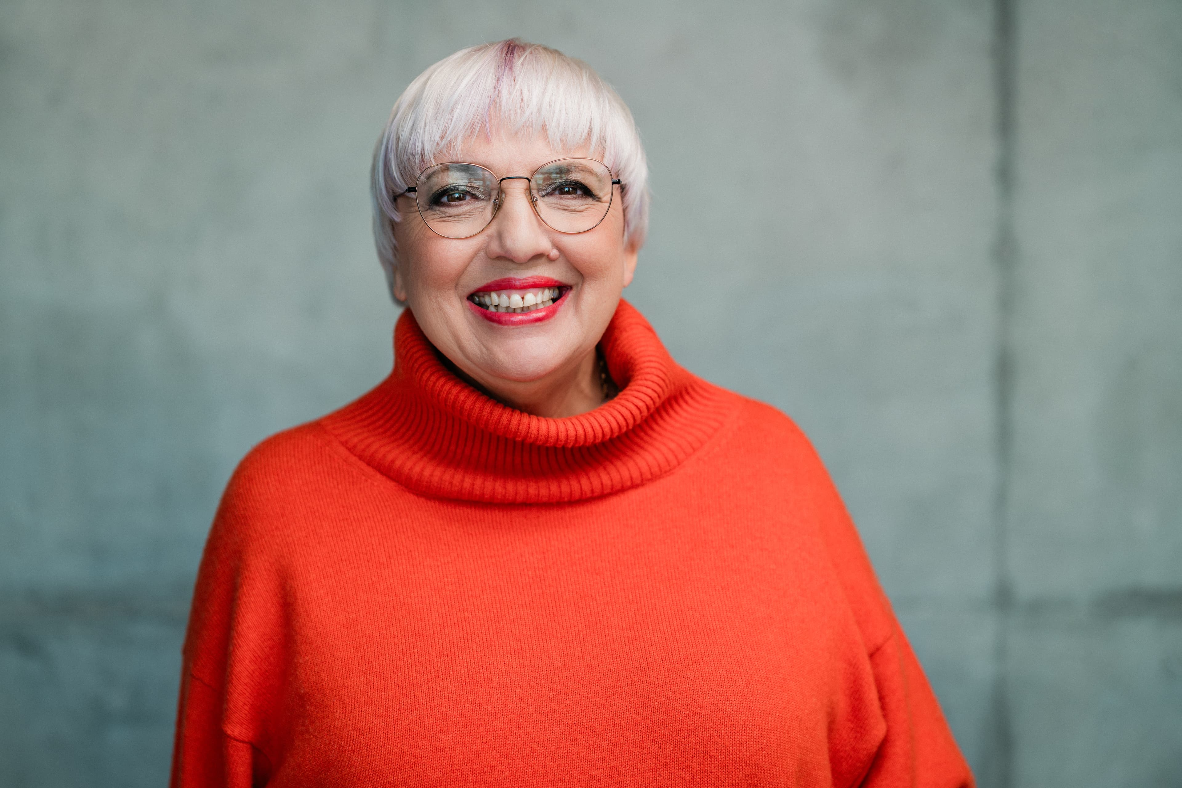 Kulturstaatsministerin Claudia Roth in einem orangenen Pulli vor grauer Wand.