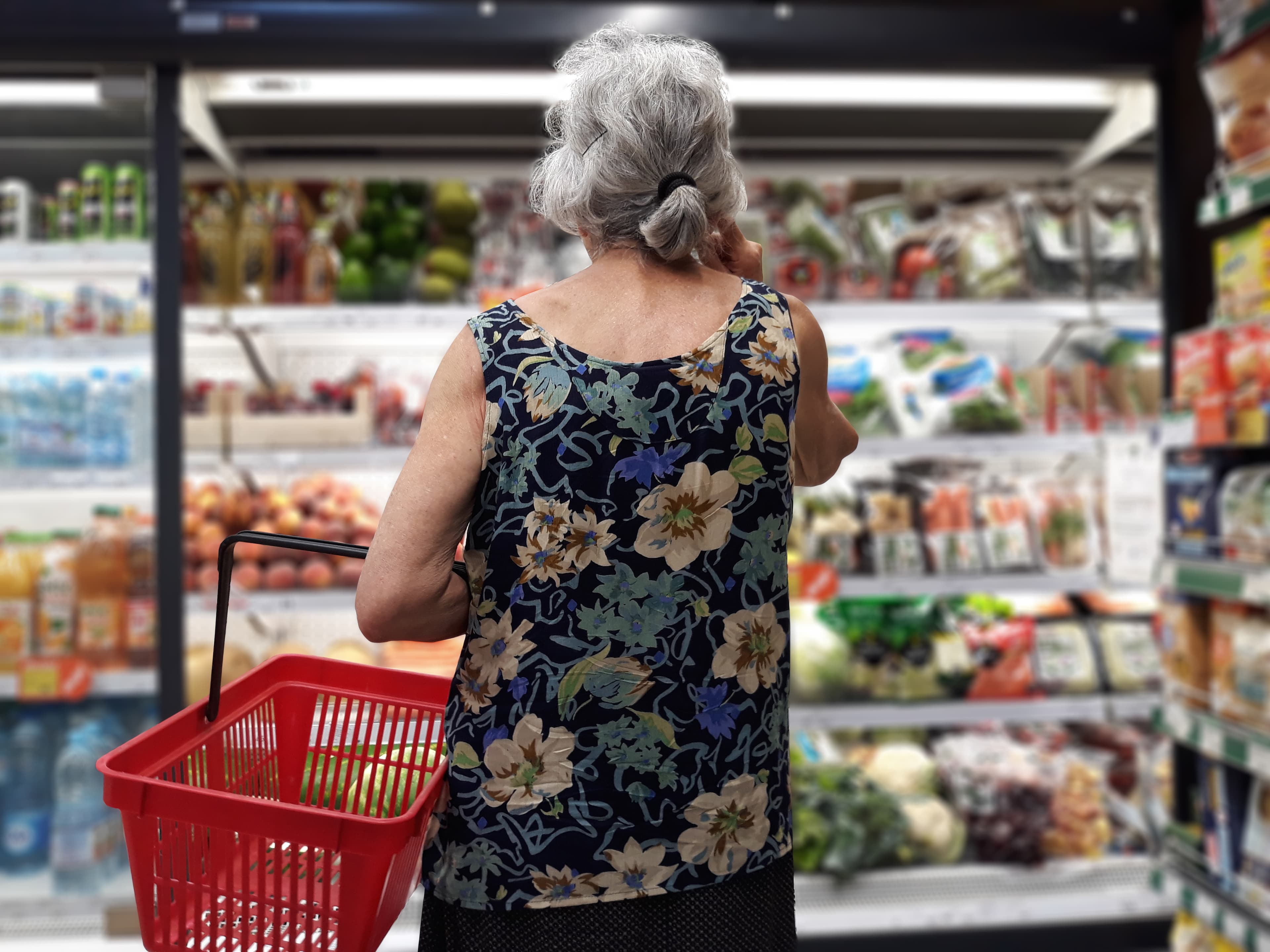Eine ältere Dame im Supermarkt schaut in das Kühlregal