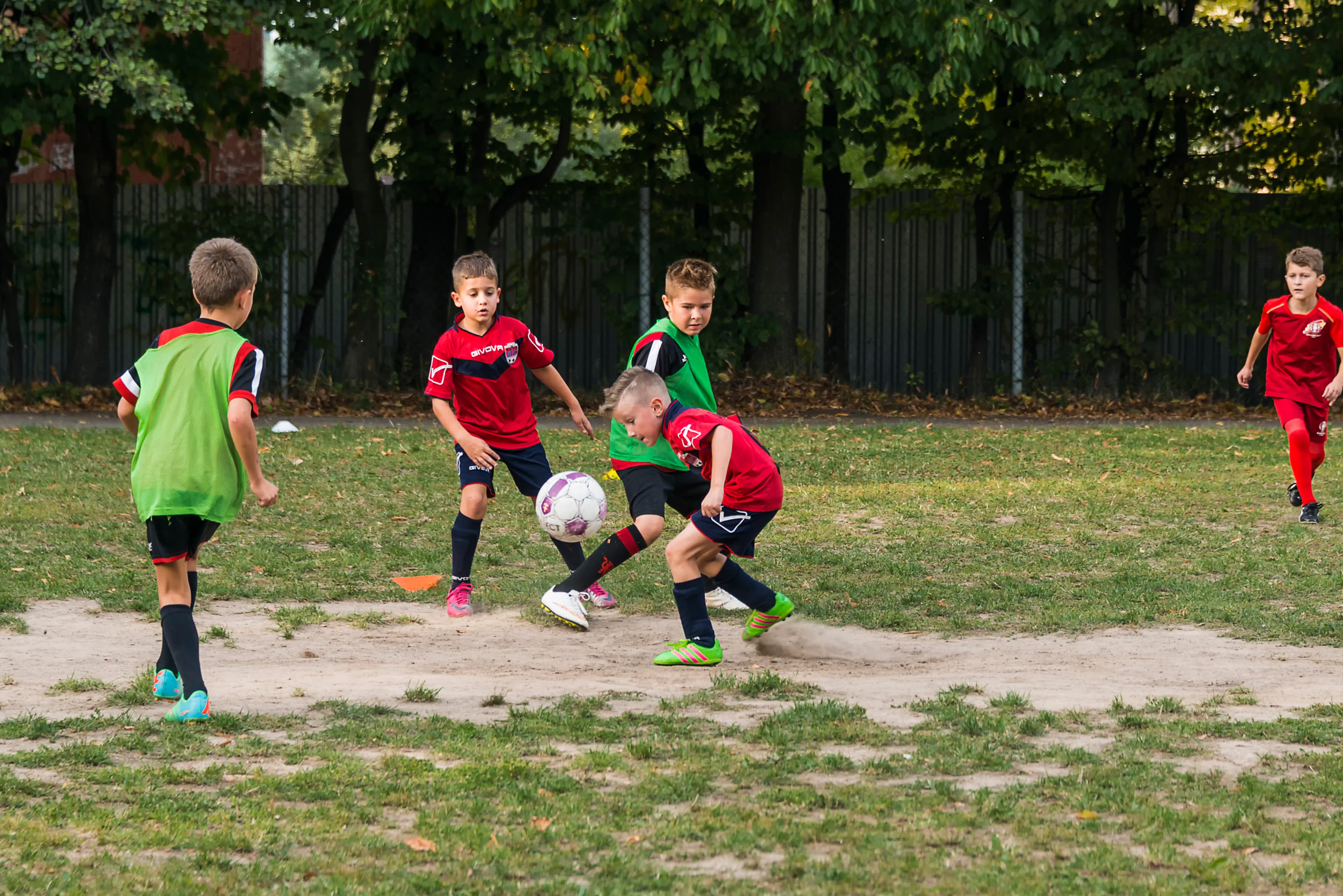 Kleine Kids spielen Fußball auf einem Bolzplatz. Sie tragen Fußballtrikots und Laibchen. Einer erkämpft sich den Ball und bereitet gerade einen Angriff vor.