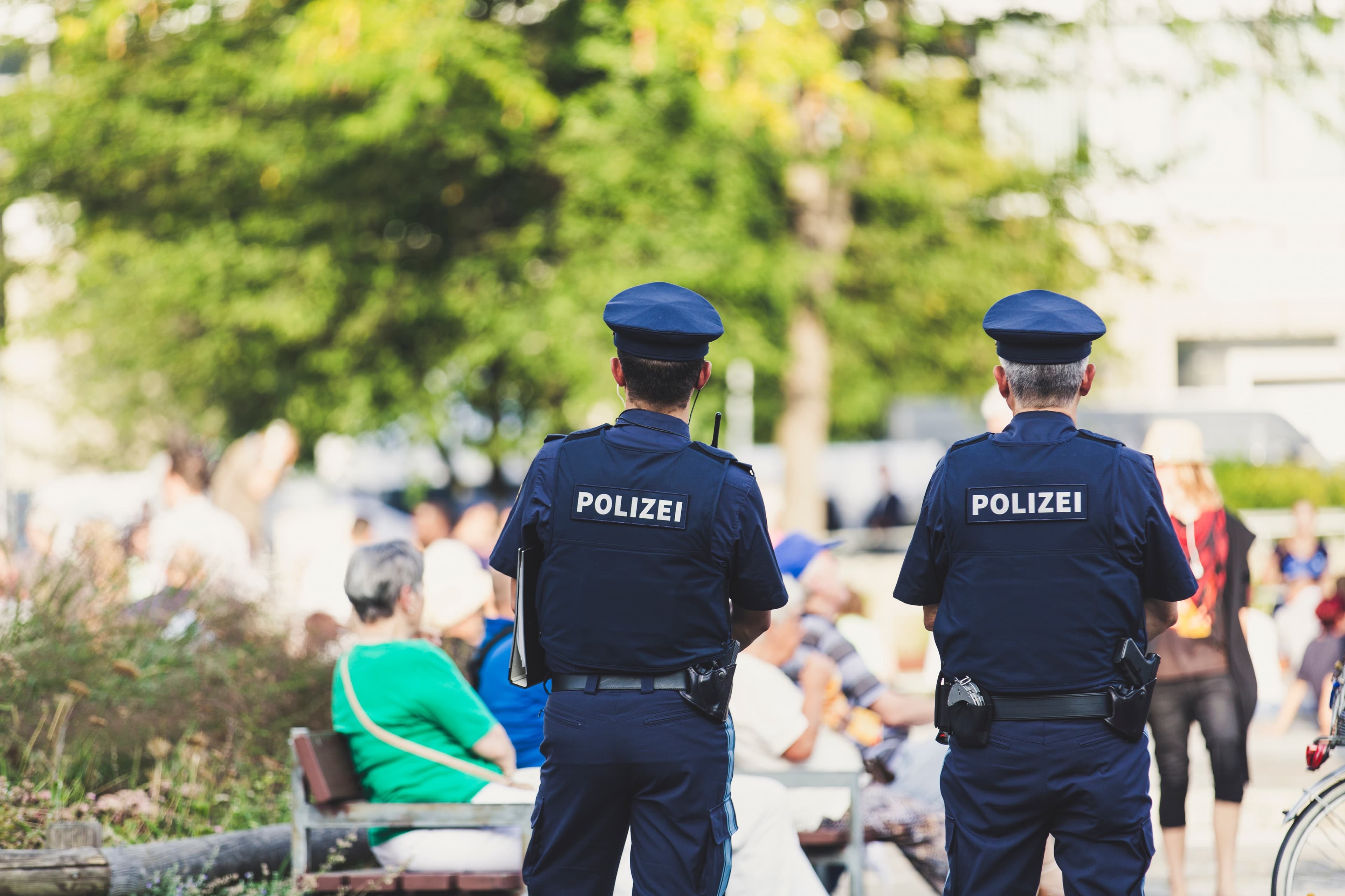 Zwei Polizist*innen stehen mit dem Rücken zum Bild gerichtet und schauen in die Richtung mehrerer Menschen.