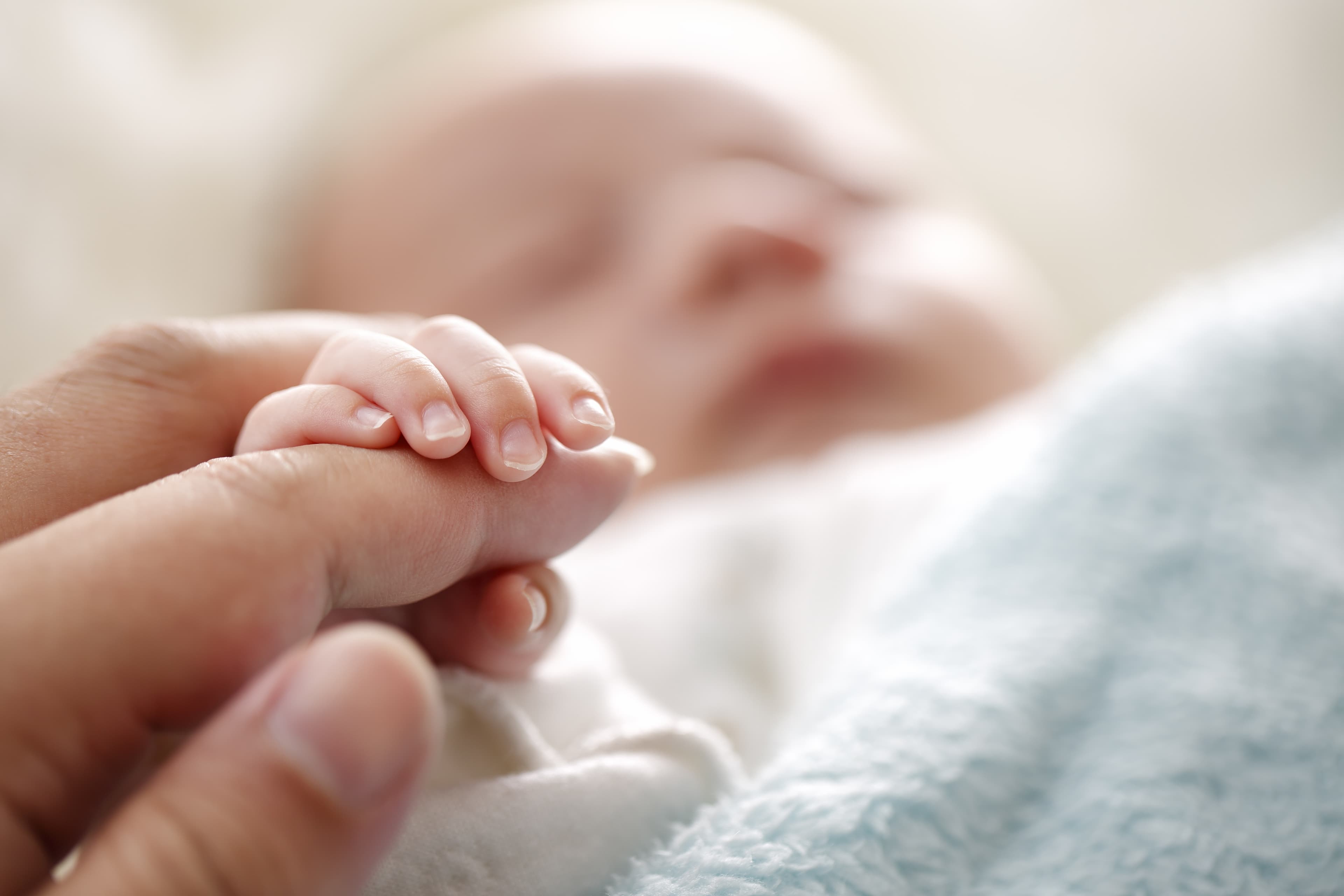 Ein Baby greift um den Finger einer Erwachsenen.