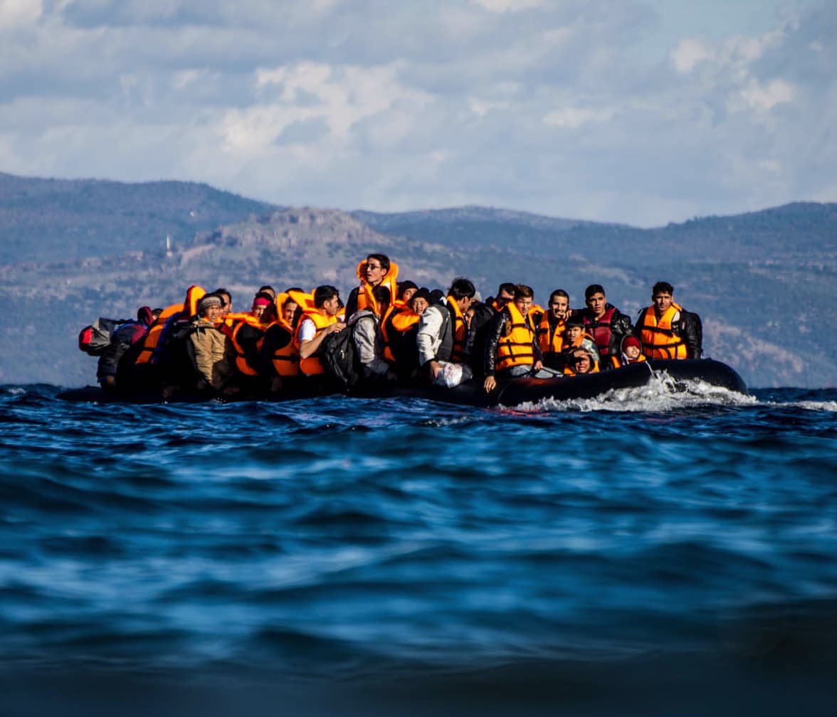 Viele Menschen in Schwimmwesten sitzen und stehen auf einem überfüllten Schlauchboot auf dem Meer.
