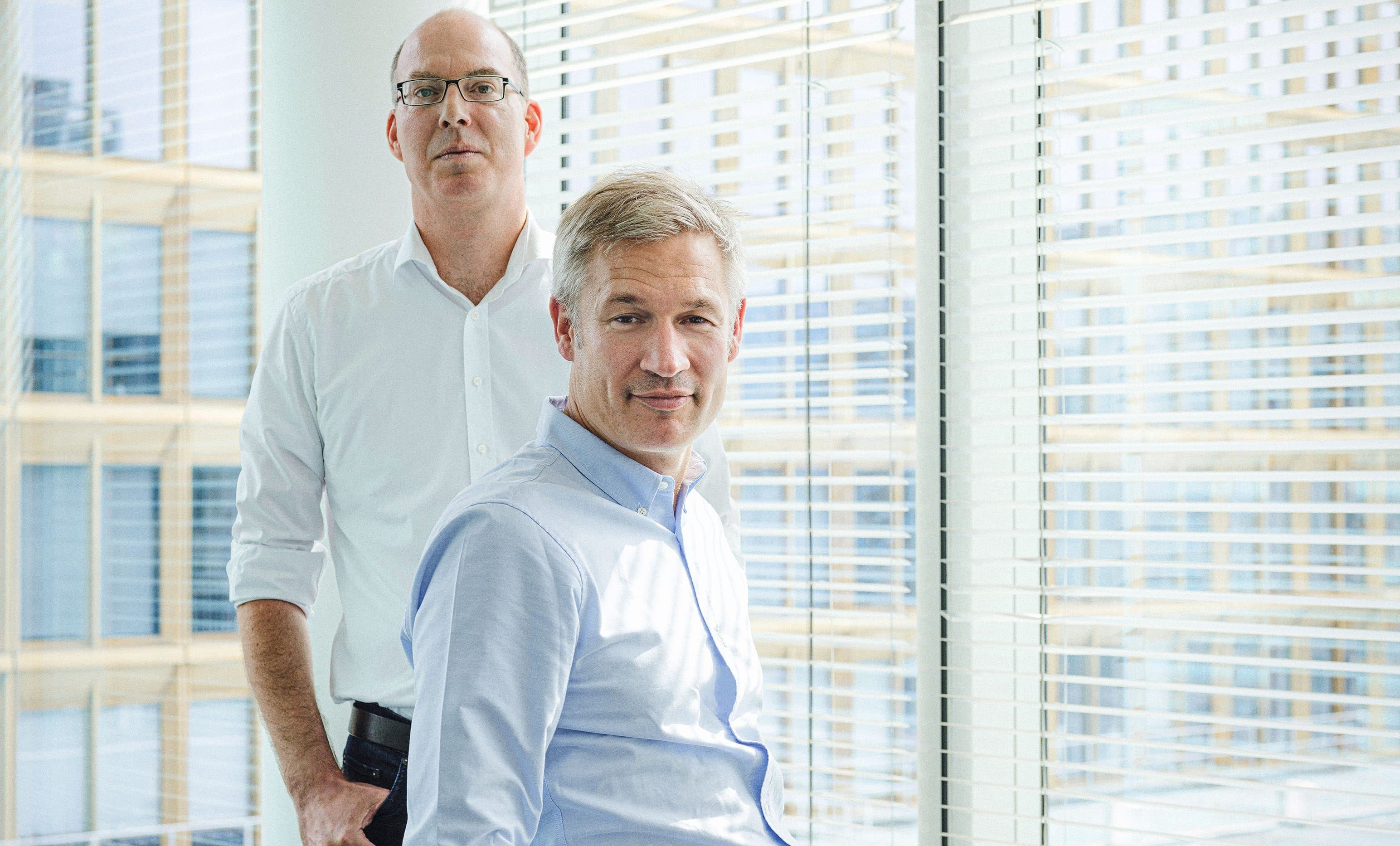 Gemeinsames Porträtfoto von Ulrich Shulte und Ulf Poschardt in einem Büro mit großen Fenstern.
