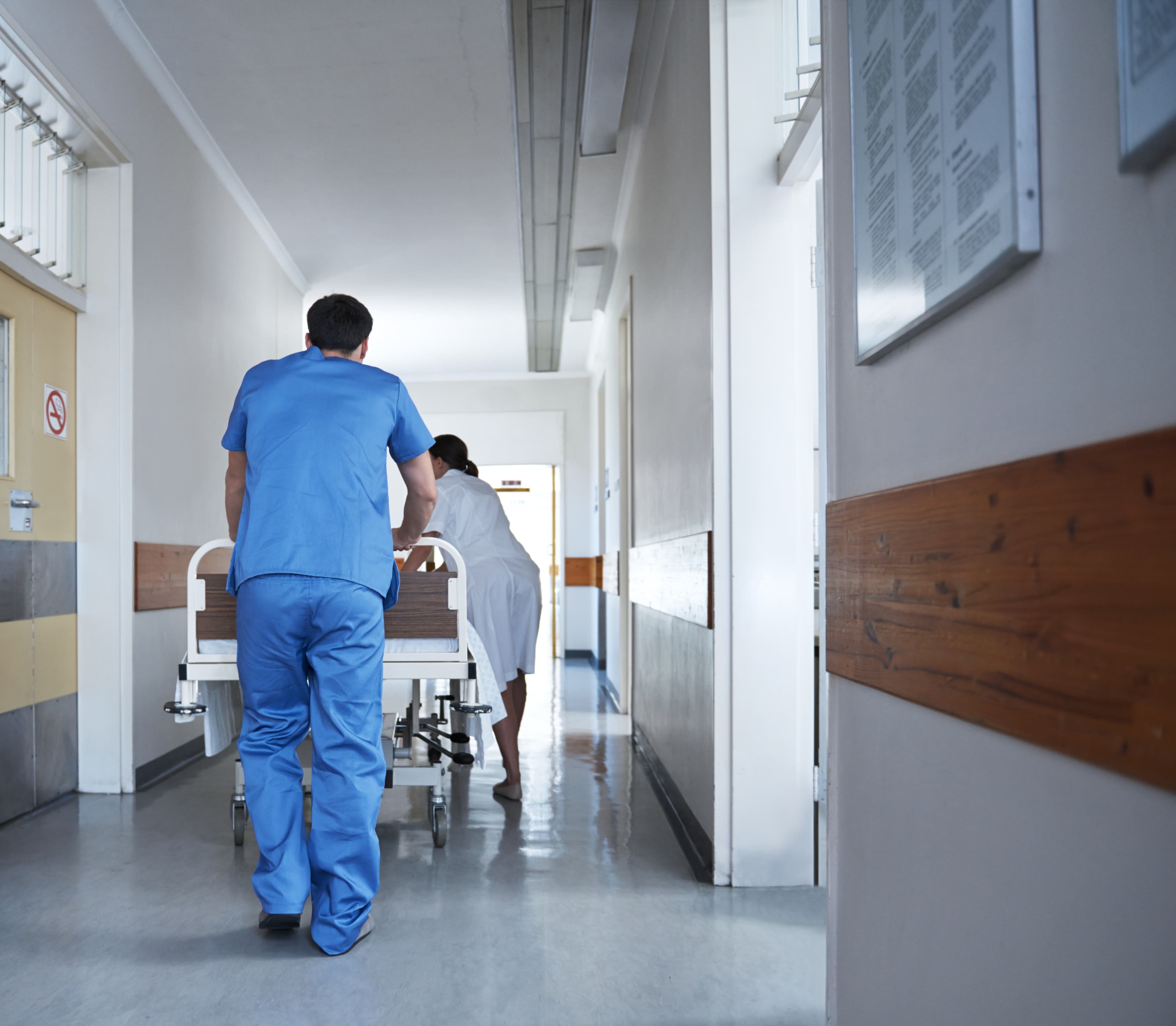 Ein Krankenpfleger und eine Krankenpflegerin schieben ein Bett durch den Krankenhausflur.