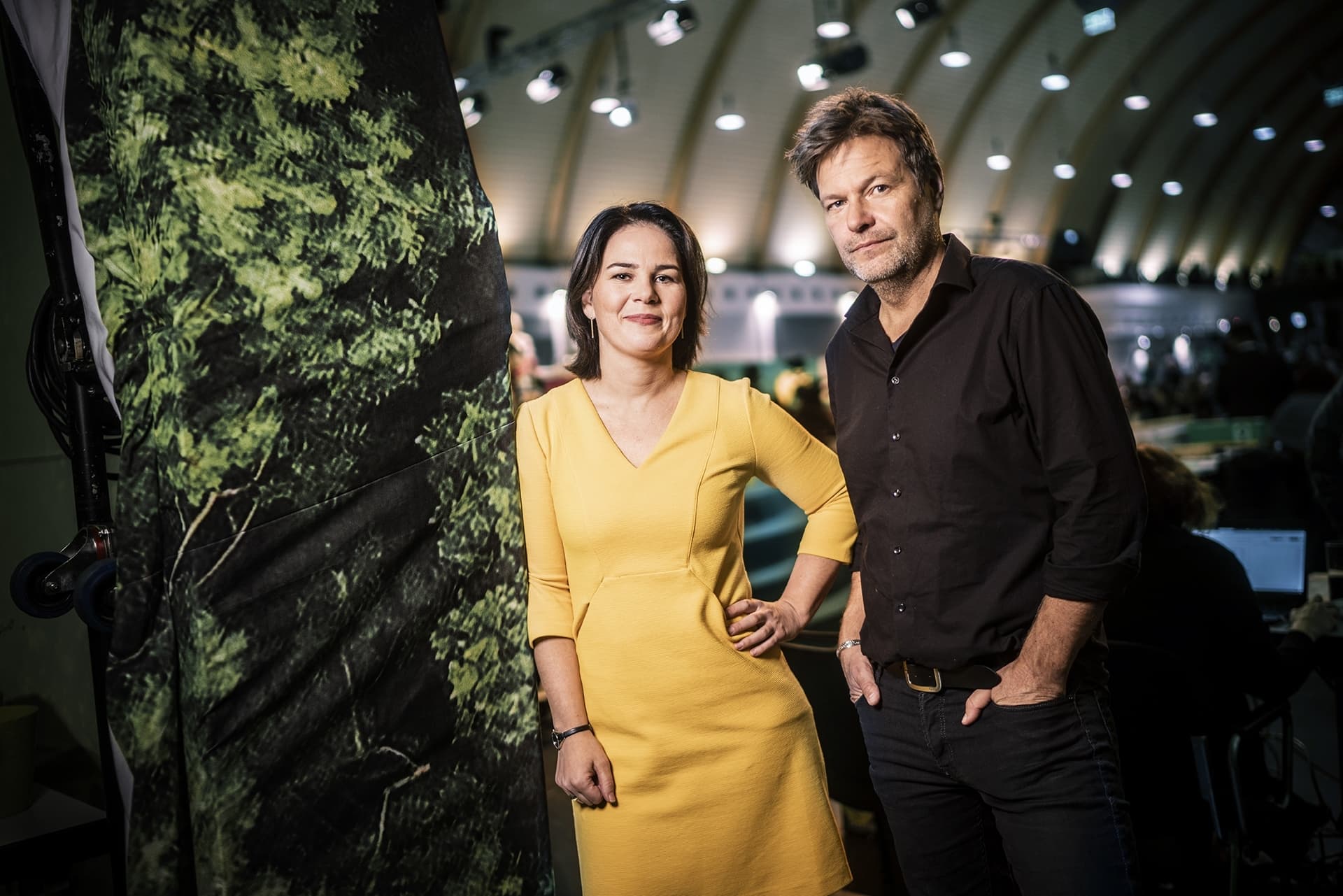 Annalena Baerbock und Robert Habeck lehnen an eine grüne Wand.