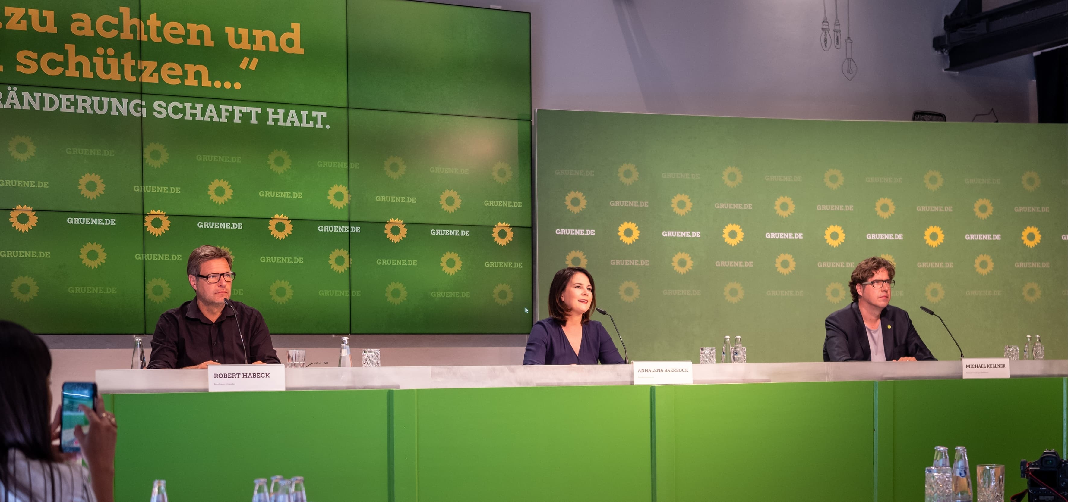 Robert Habeck, Annalena Baerbock und Michael Kellner sitzen vor einer grünen Wand bei einer Pressekonferenz.