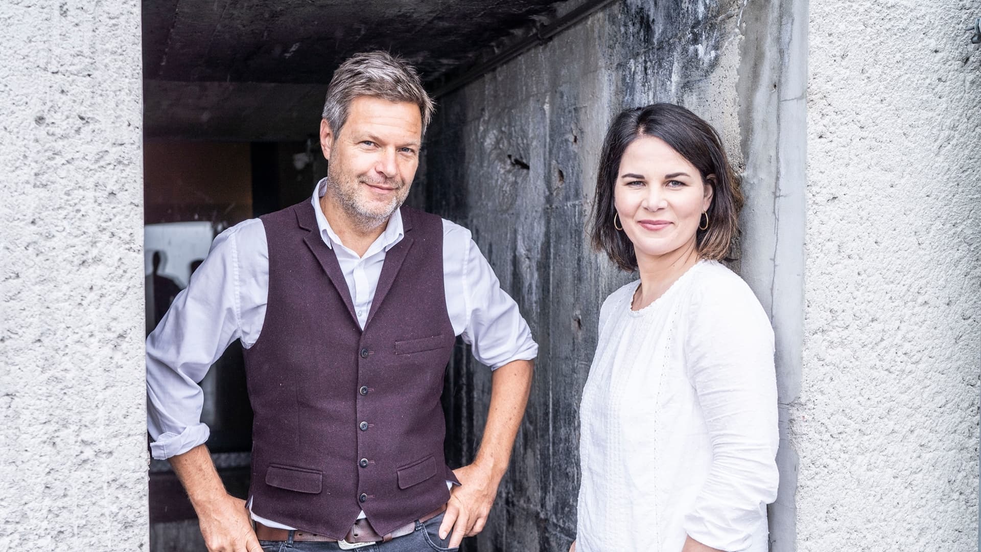 Die Bundesvorsitzenden von BÜNDNIS 90/DIE GRÜNEN Robert Habeck und Annalena Baerbock stehen vor einer grauen Betonwand, rechts und links von ihnen sieht man auch Beton.