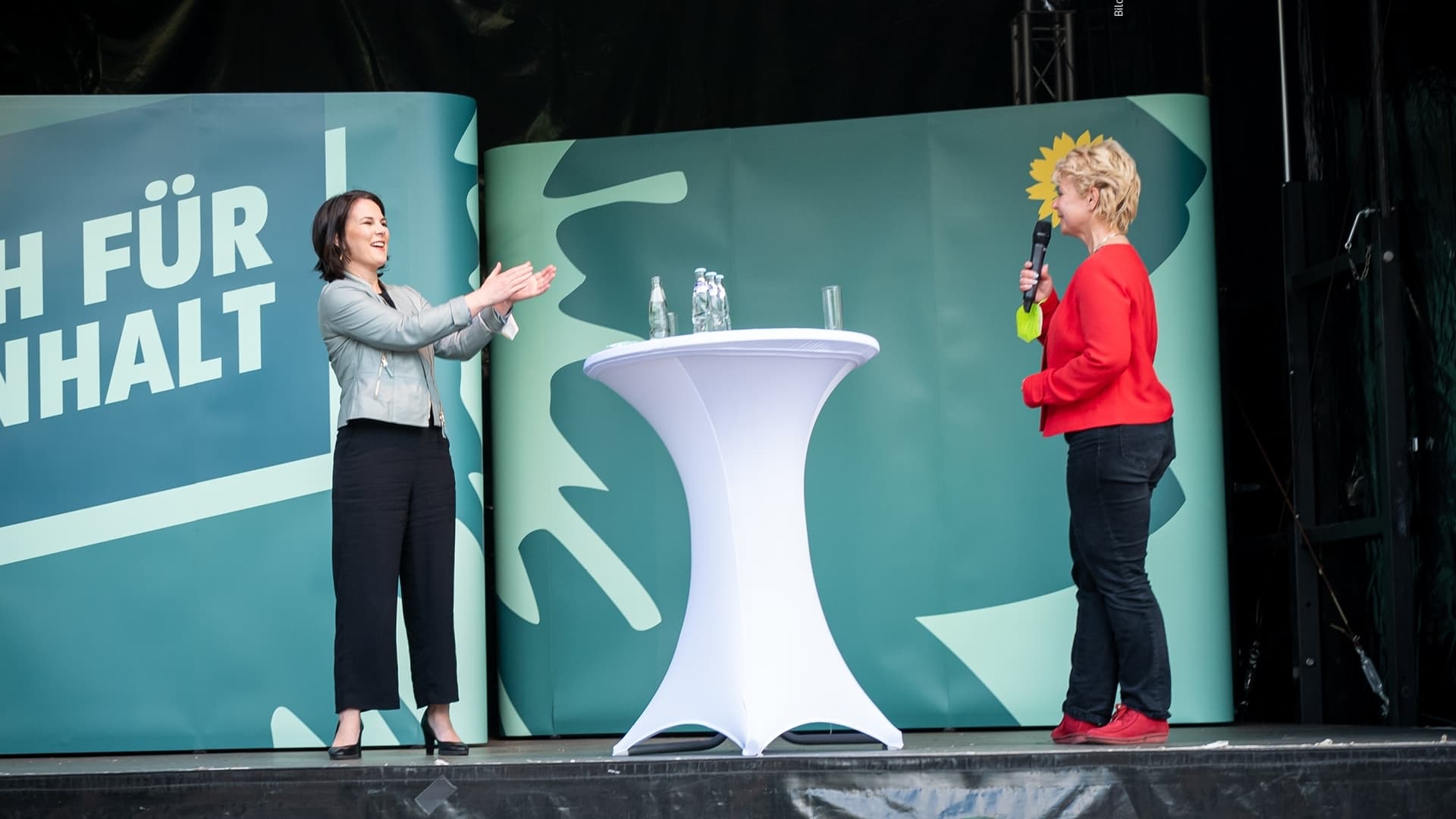 Annalena Baerbock steht rechts auf einer Bühne und applaudiert Conny Lüddemann, die links auf der Bühne steht.