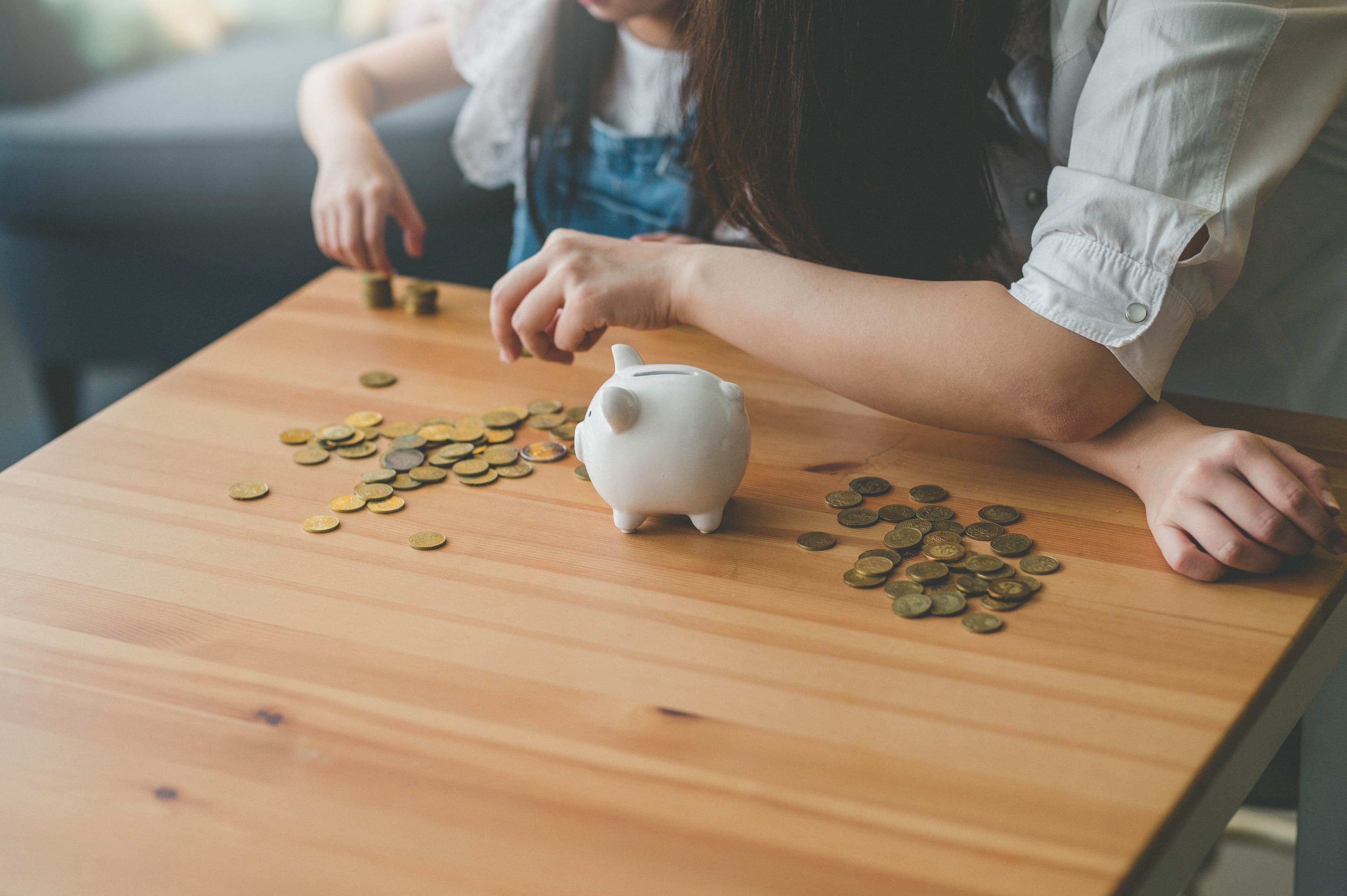 Man sieht wie eine erwachsene Person zusammen mit einem Kind auf dem Couchtisch Geld aus dem Sparschwein zählt.