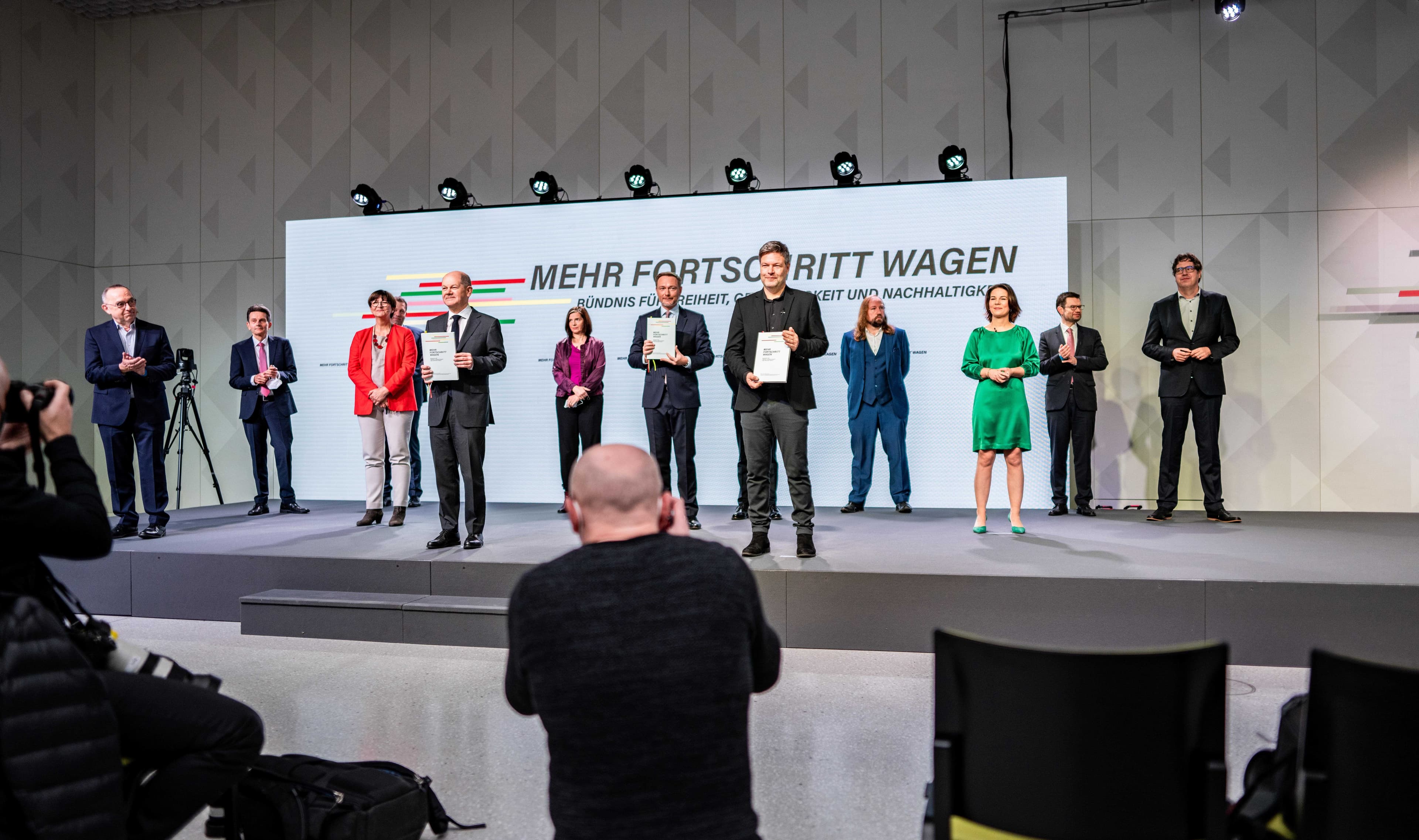 Vertreter*innen der neuen Regierungsparteien bei der Unterzeichnung des Koalitionsvertrags: Sie stehen auf der Bühne vor einer Pressewand mit der Aufschrift: "Mehr Fortschritt wagen"