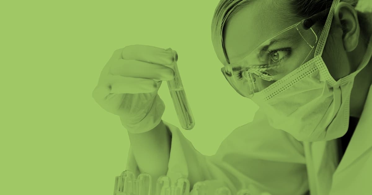 Eine junge Frau trägt eine Schutzbrille und hält ein Reagenzglas in die Luft