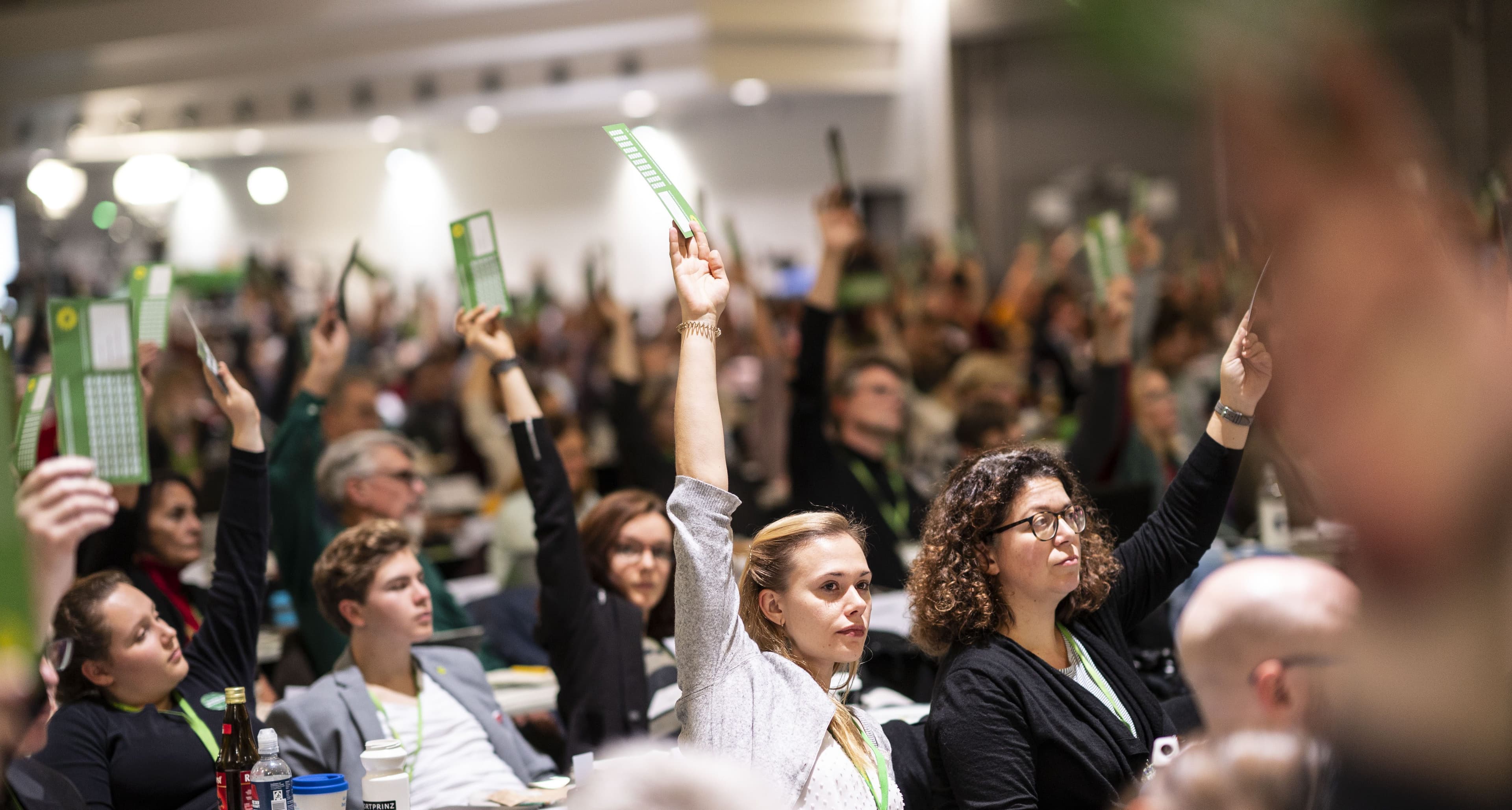 Mehrere Delegierte sitzen in mehreren Tischreihen und halten jeweil eine grüne Karte zur Abstimmung hoch.
