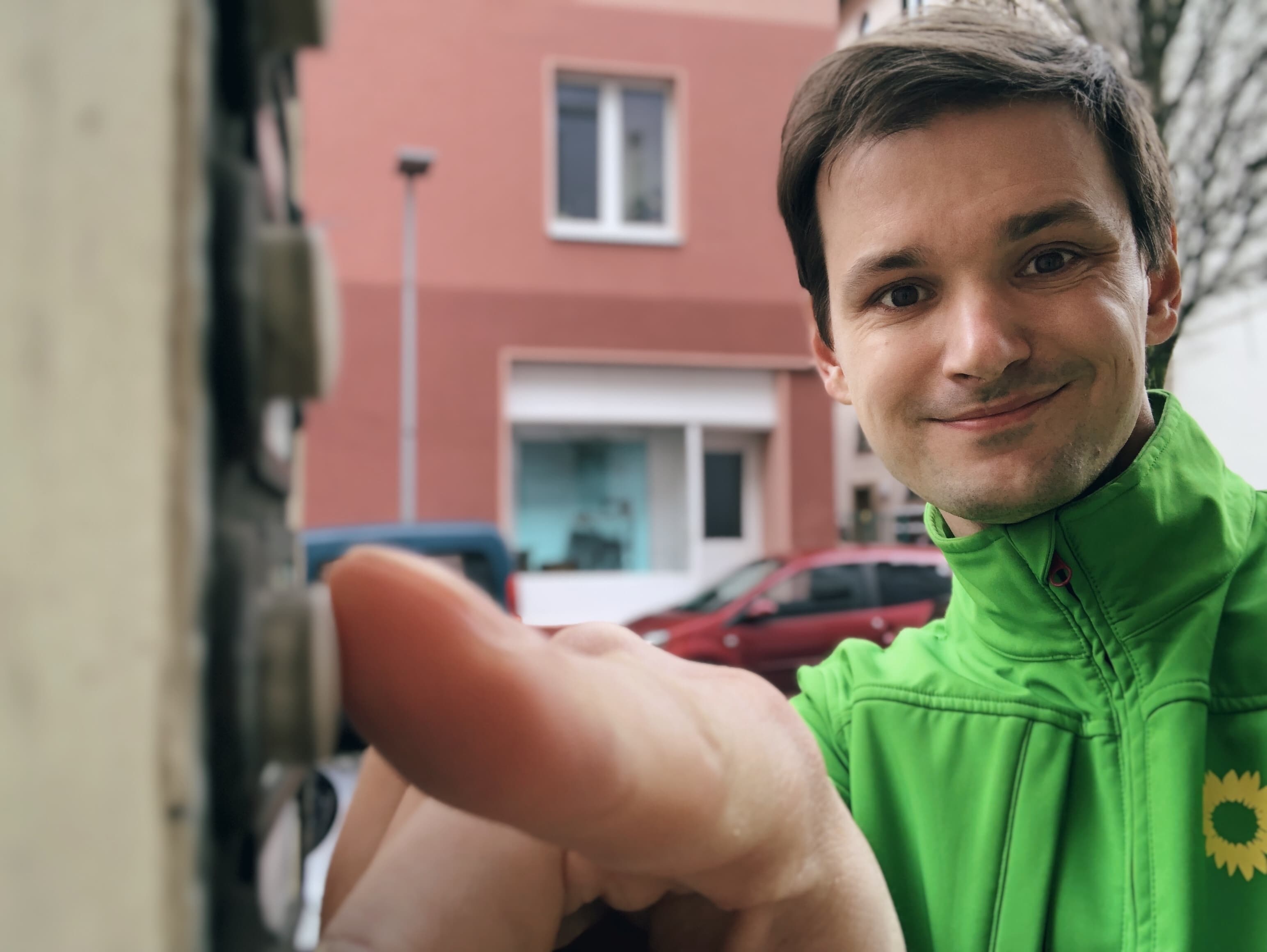 Porträt einer Person, die auf ein Klingelschild drückt und lächelt.