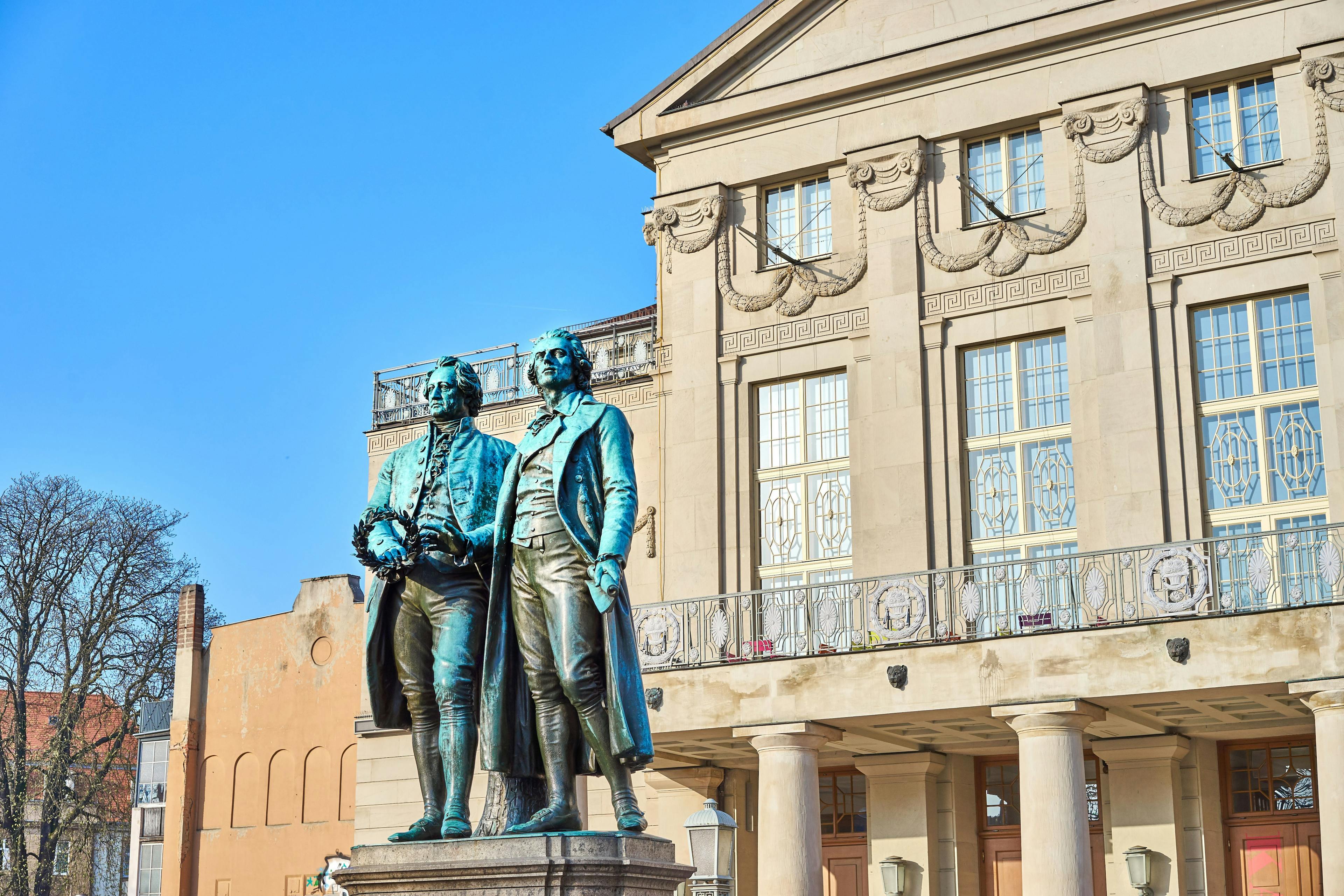 Bronze-Statue mit zwei Männern vor einem Theater.