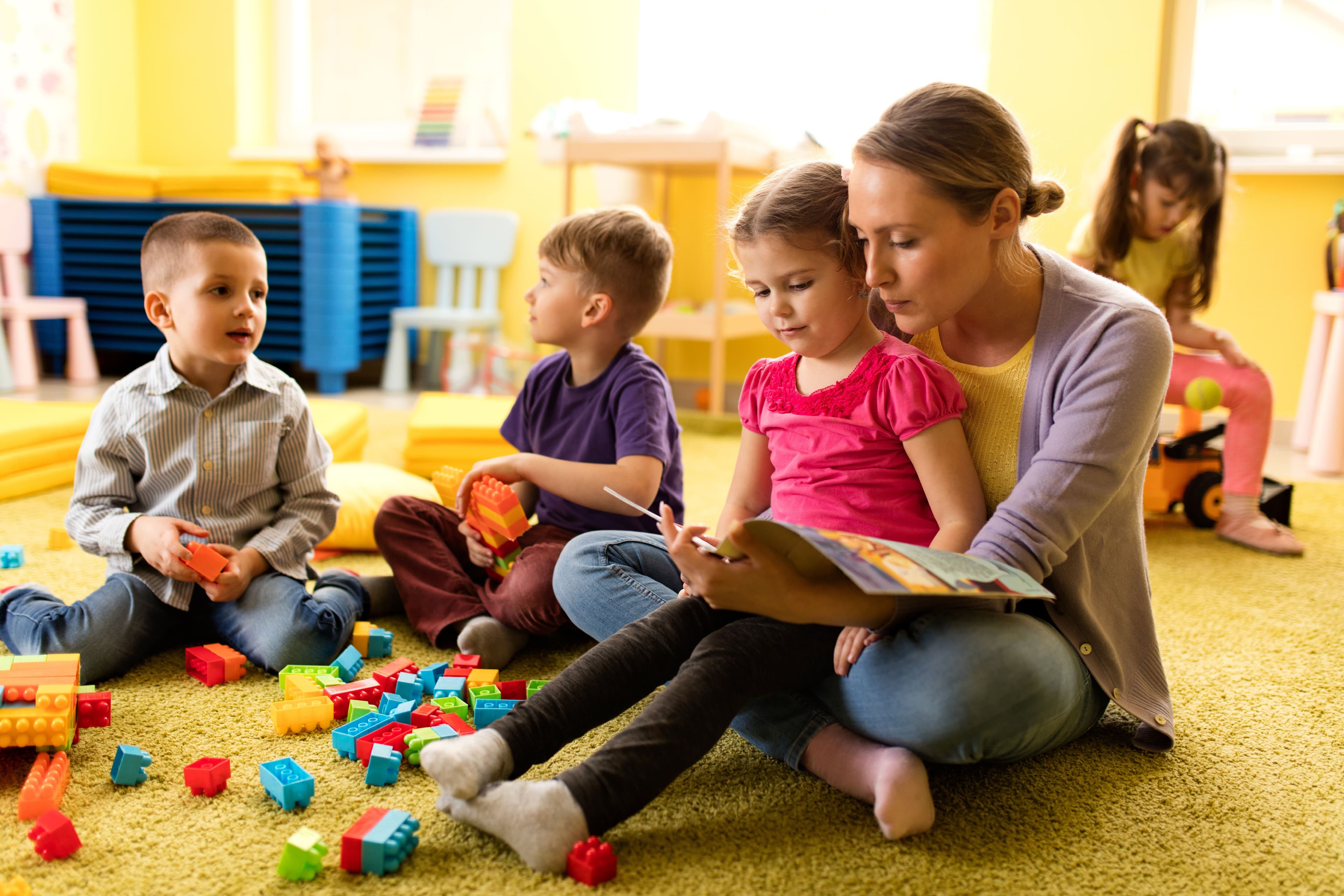 Eine Frau sitzt mit vier Kindern auf dem Fußboden und liest aus einem Buch vor.