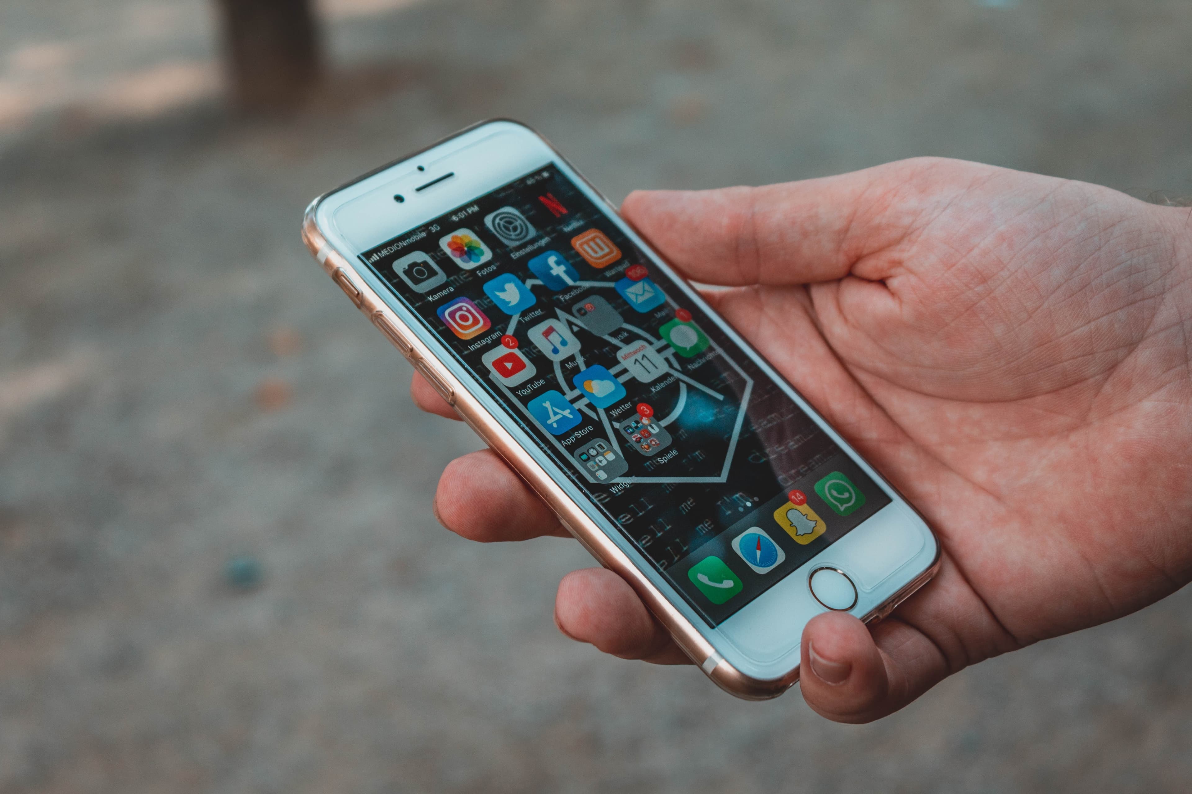 Eine Hand hält ein Smartphone - der Startbildschirm mit diversen Apps ist zu sehen.