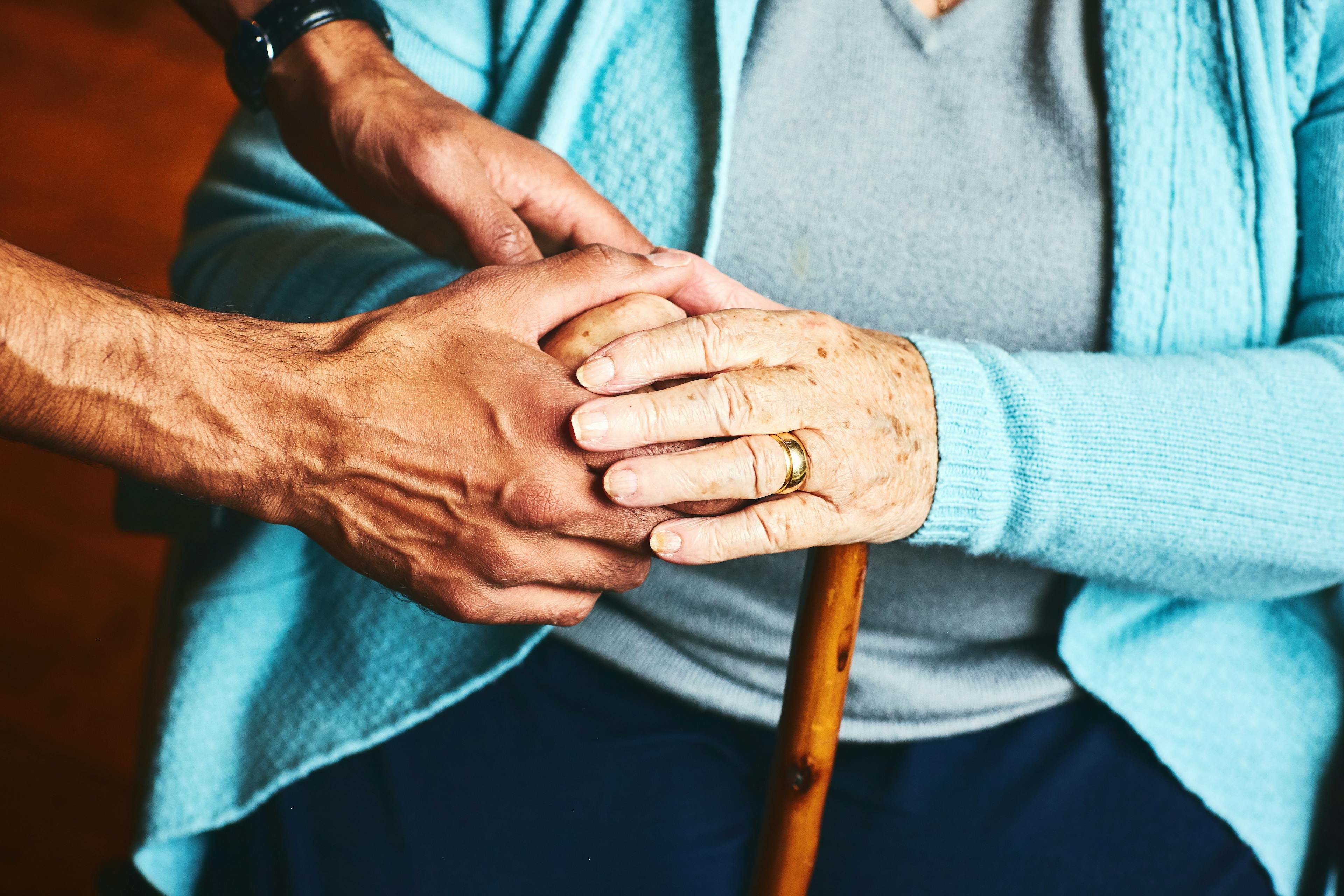 Die Hände einer sitzenden älteren Frau sind zu sehen und werden von zwei Händen einer Pflegekraft gehalten.
