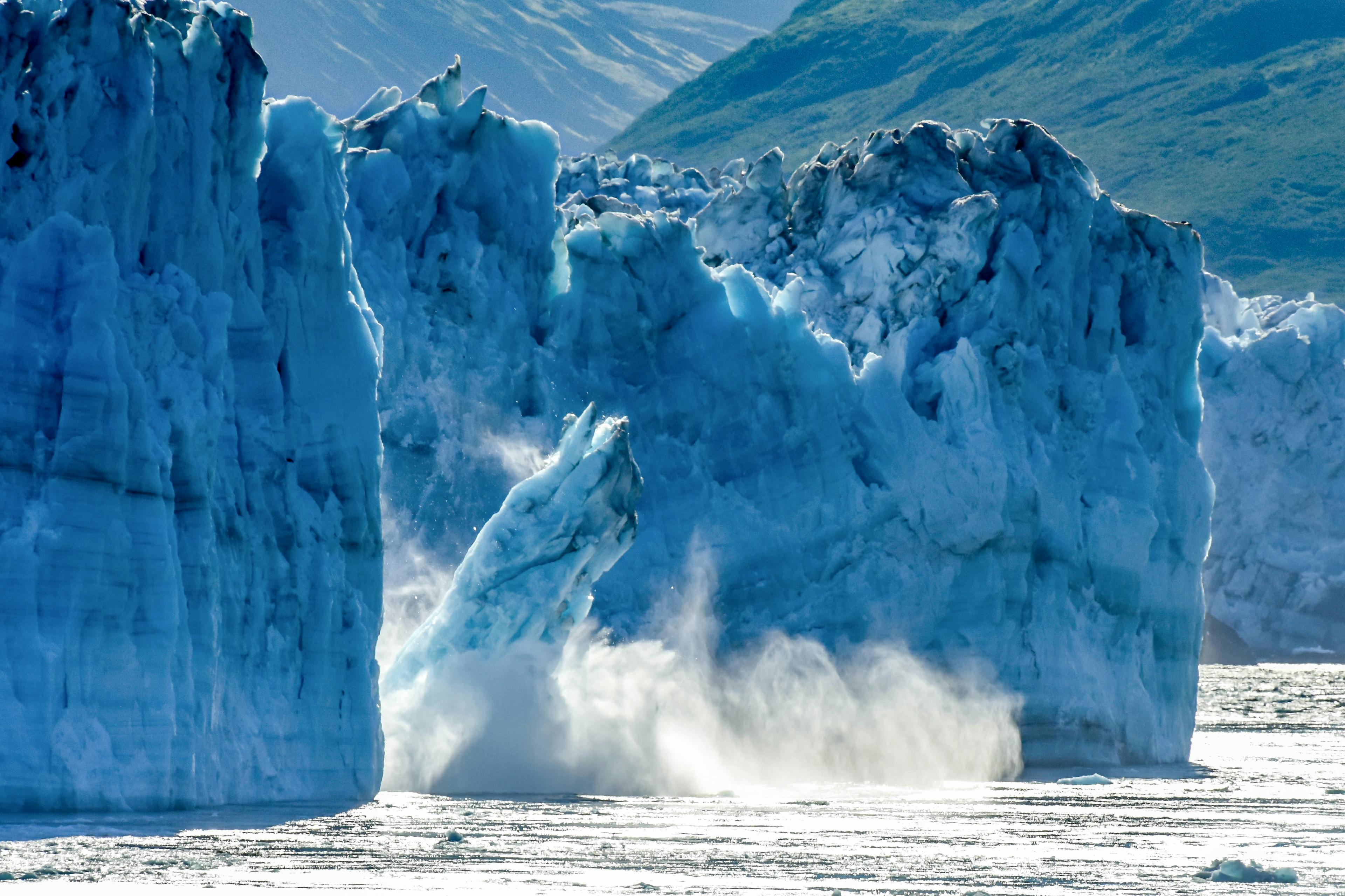 Aus einem großen Gletscher bricht ein großes Gletscherstück ab und fällt ins Wasser.