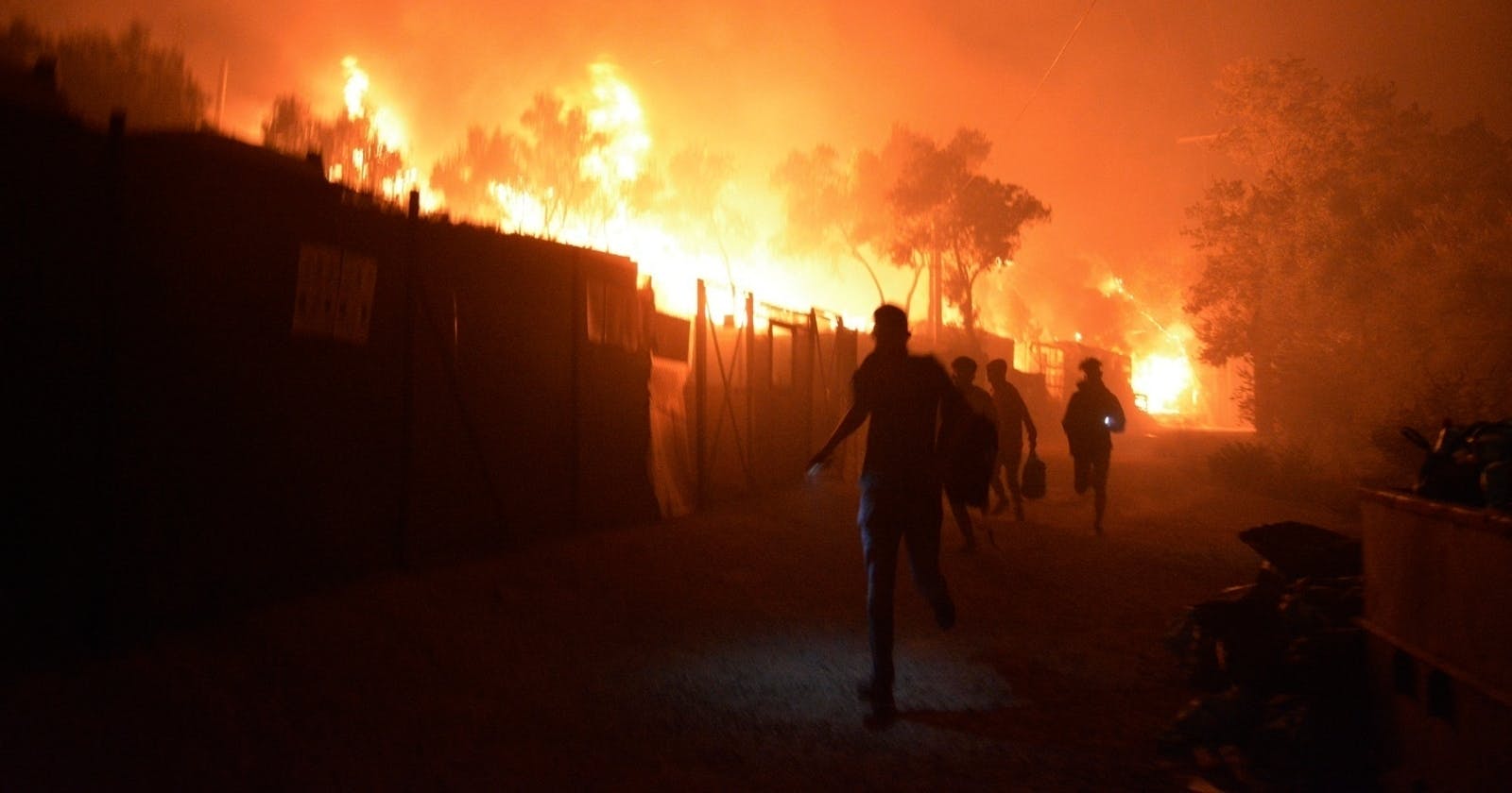 Man sieht Beretterverschläge in der Nacht, die in Flammen stehen. Davor die Silhouetten von fliehenden Menschen.