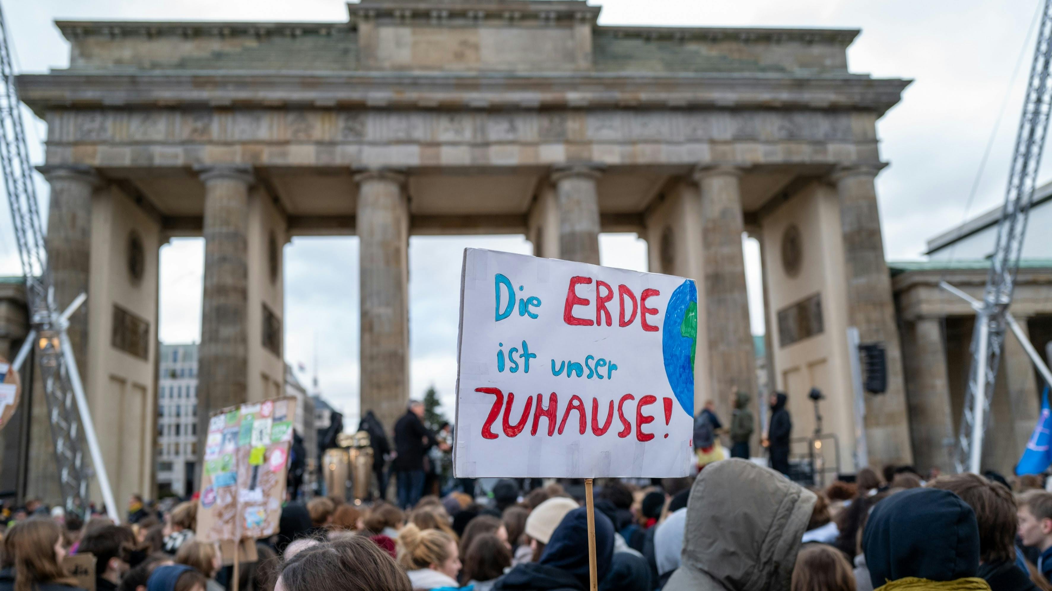 Eine Demo vor dem Brandenburger Tor, man sieht die Köpfe der Demonstrant*innen und ein Schild: "Die Erde ist unser ZUHAUSE!"