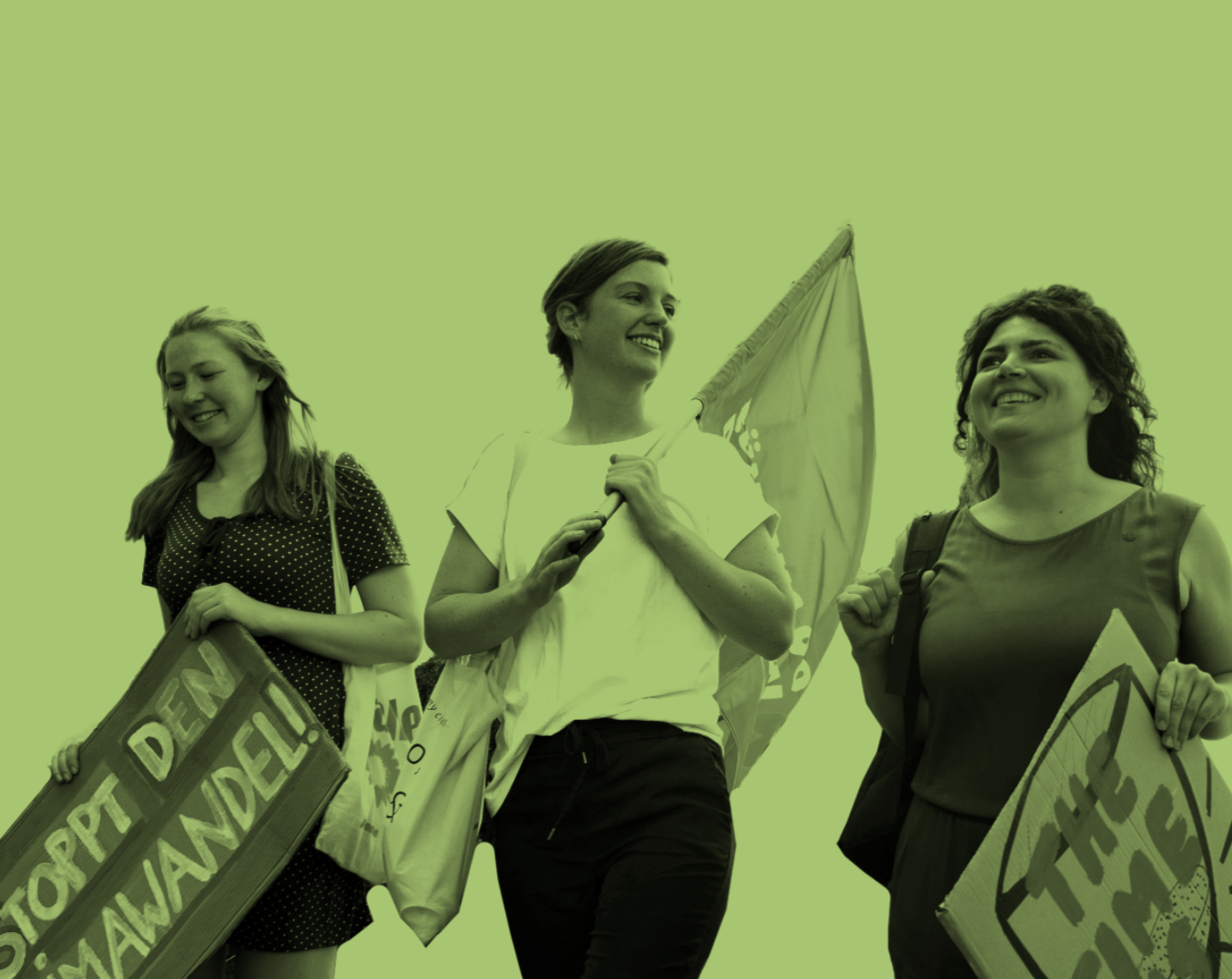 Drei junge Frauen gehen nebeneinander und lachen. Sie tragen Fahnen und Transparente, auf denen steht: "Stopp den Klimawandel!" und "The Time is Now"