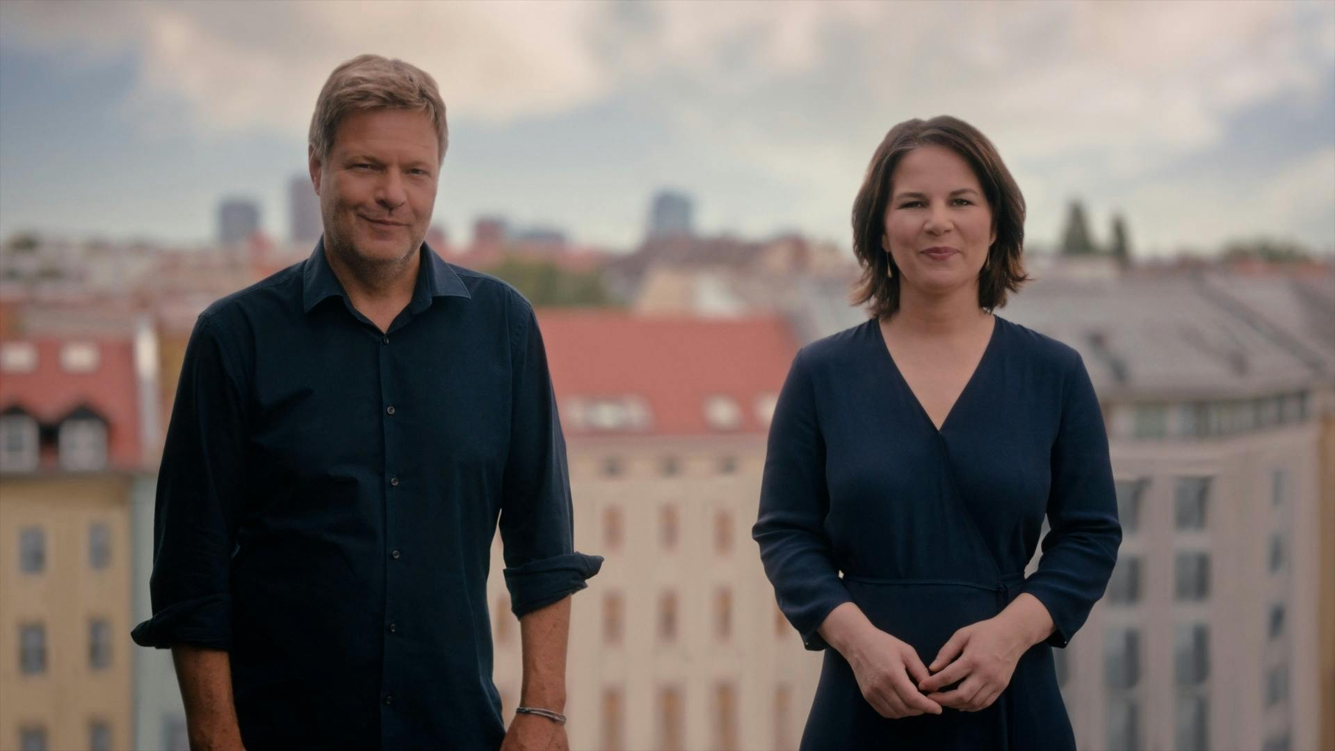 Robert Habeck und Annalena Baerbock stehen vor Häuserfassaden und lächeln in die Kamera.