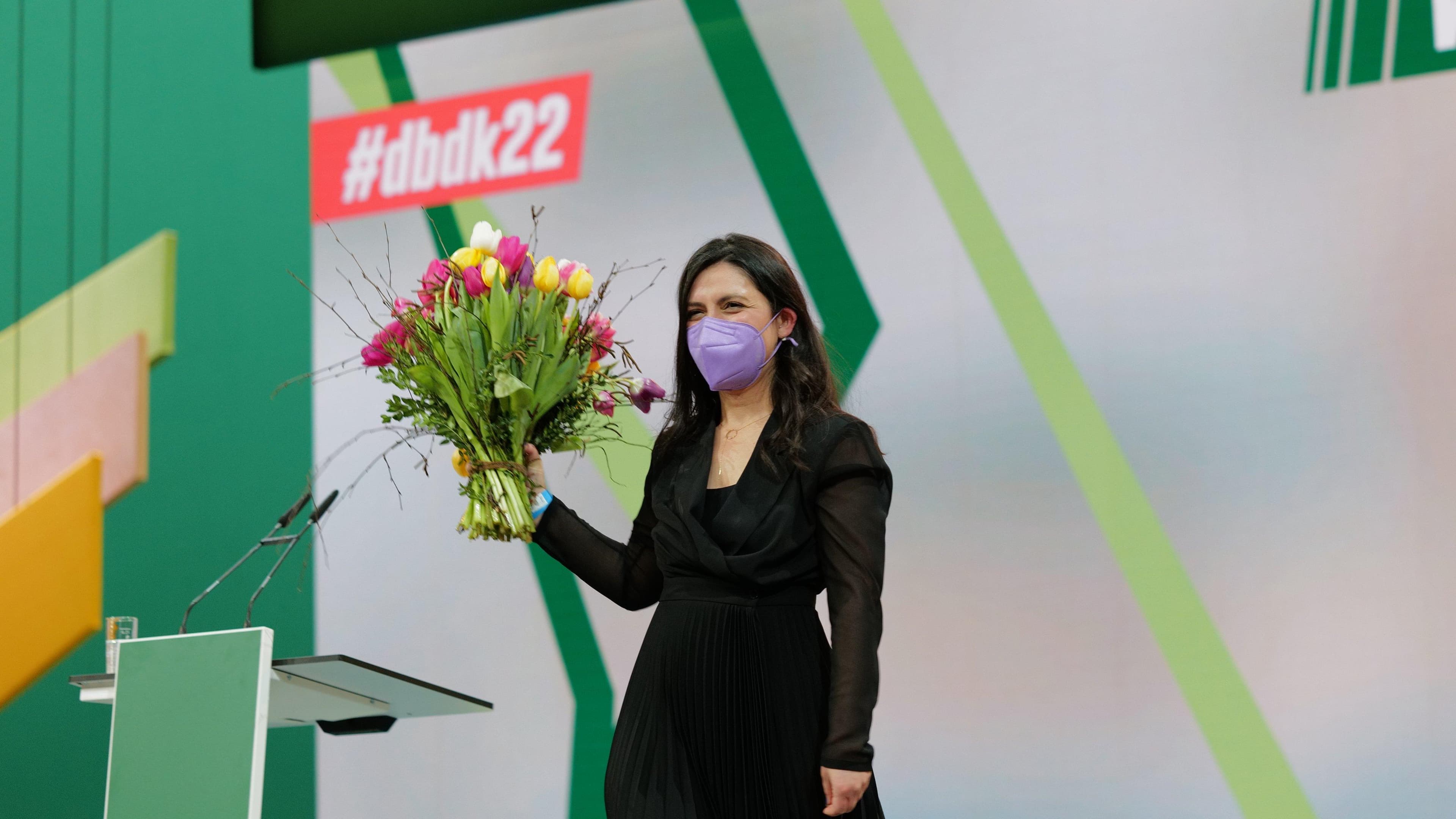 Pegah Edalatian steht hinter einem Redner*innnpult und hält einen Strauß Tulpen hoch