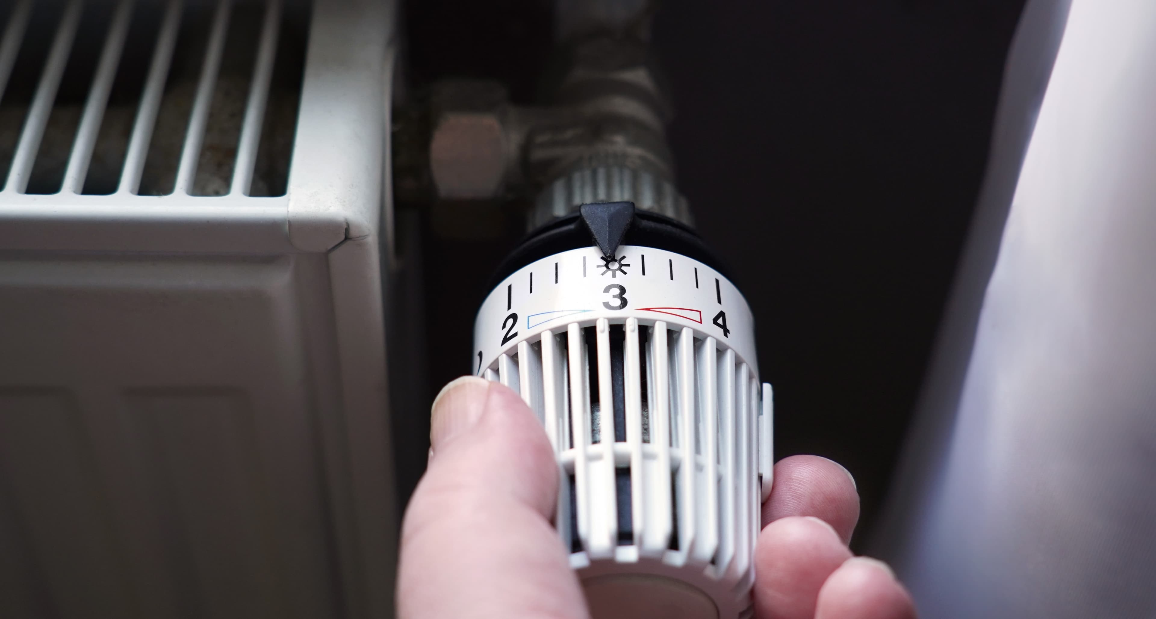 Bildausschnitt einer Heizung und einer Hand, die am Regler dreht