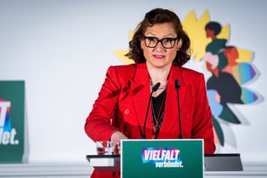 Ferda Ataman steht im roten Jackett hinter einem Redner*innenpult mit der Aufschrift "Vielfalt verbündet" und spricht ins Mikrofon.