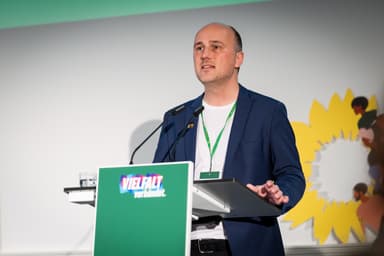 Sven Lehmann steht hinter einem grünen Redner*innenpult mit der Aufschrift "Vielfalt verbündet"