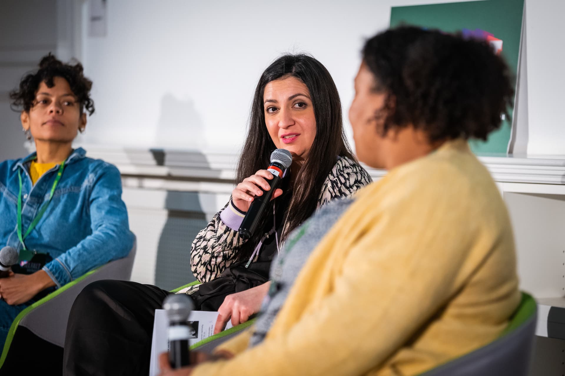 Pegah Edalatian sitzt zwischen zwei Frauen und hat ein Mikrofon in der Hand, in das sie spricht.