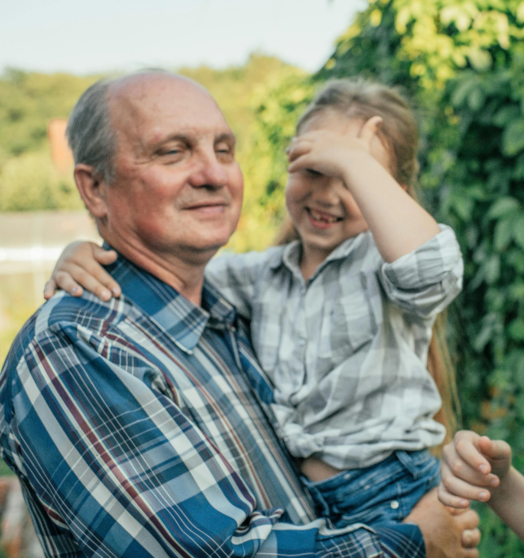 Ein Großvater mit Enkelin auf dem Arm in der Natur.