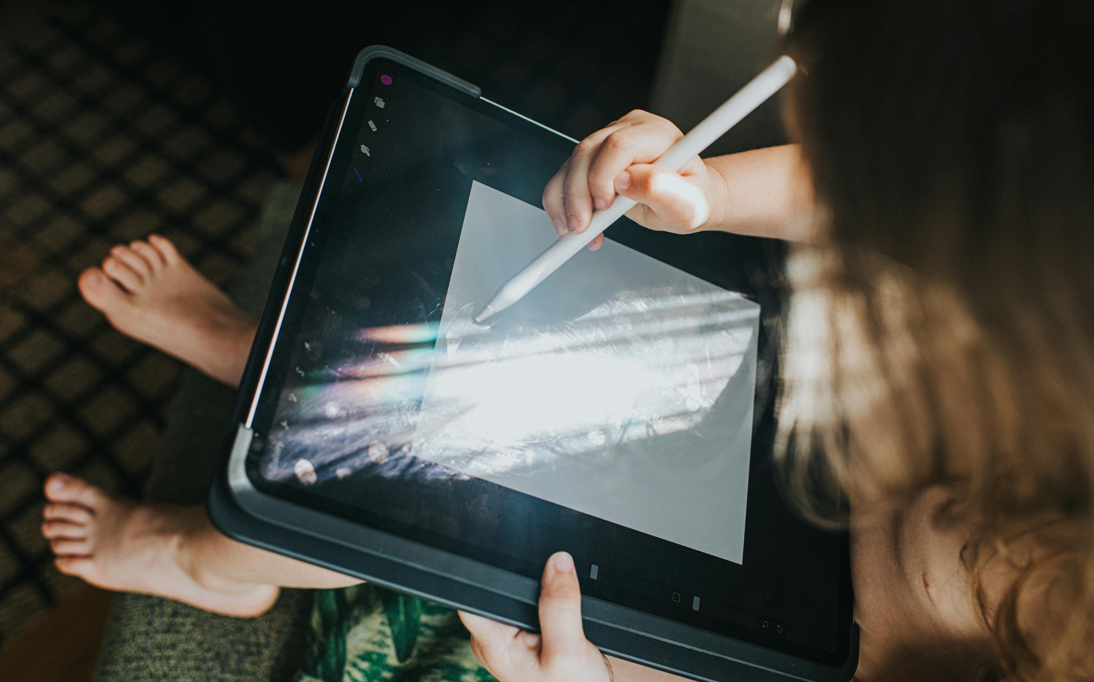 Ein Kind malt mit einem digitalen Stift auf einem Tablet.