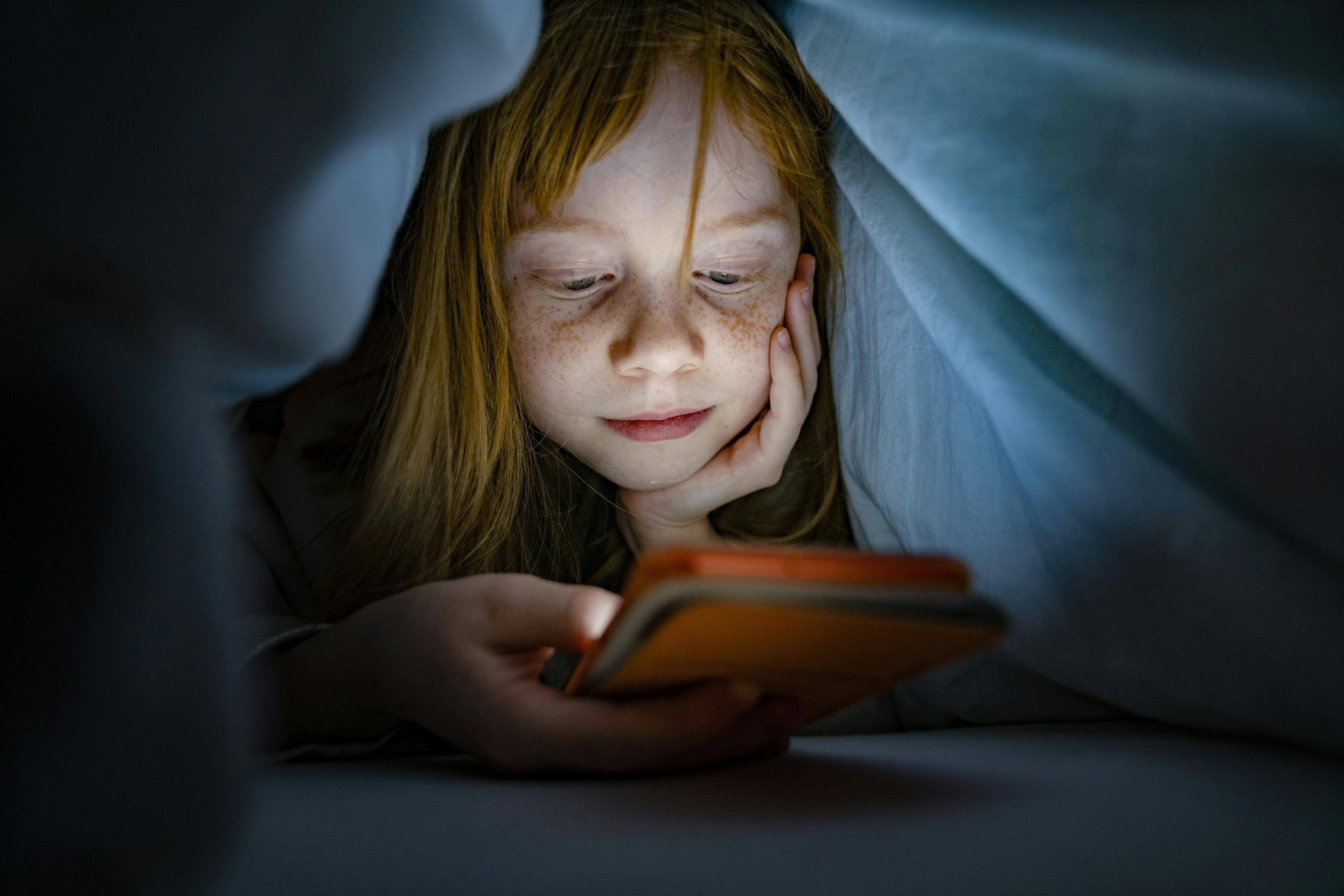 Ein Mädchen liest auf einem E-Reader unter einer Decke.
