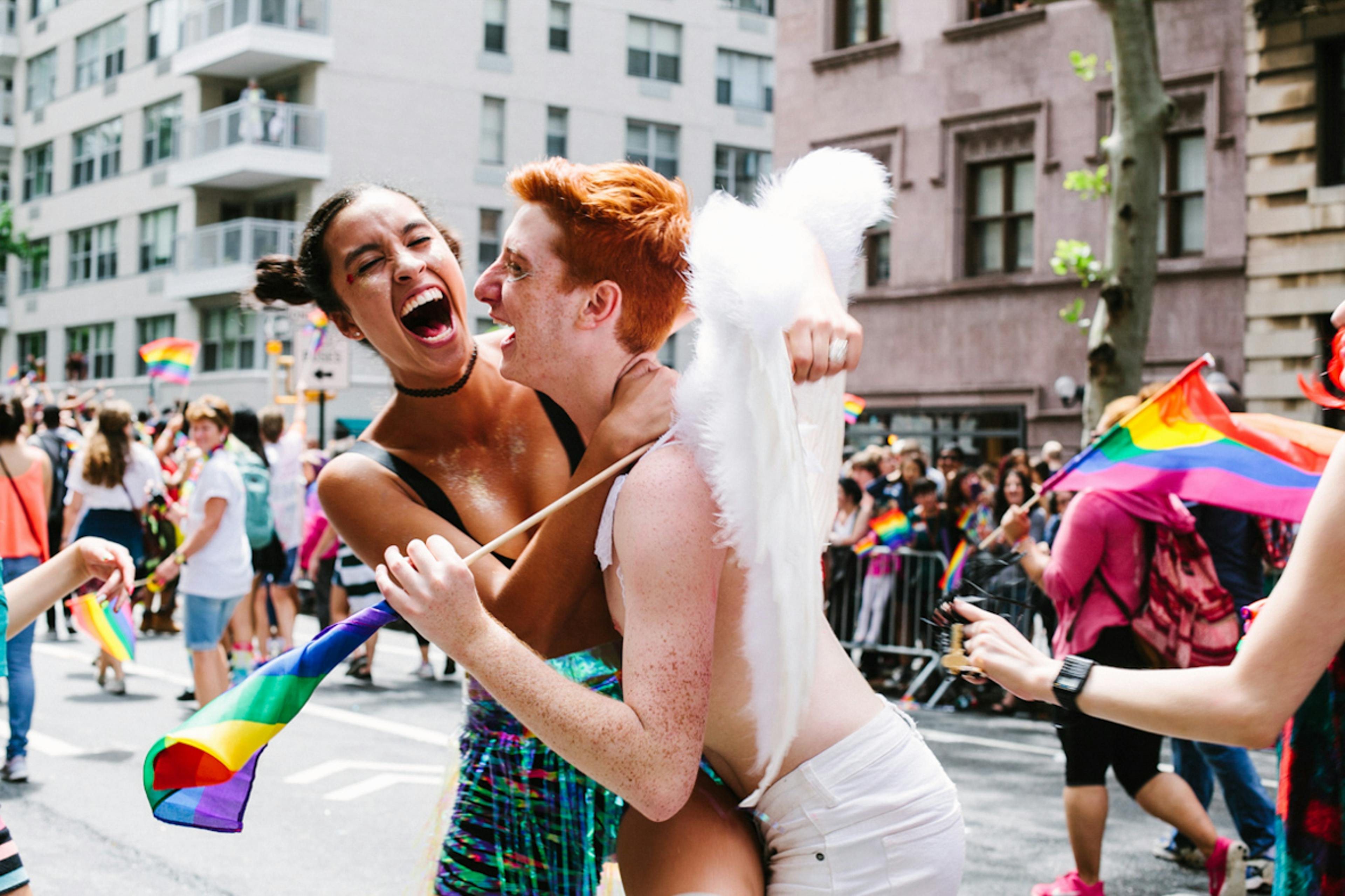 Zwei junge Menschen liegen sich lachend in den Armen bei einer Pride Parade.