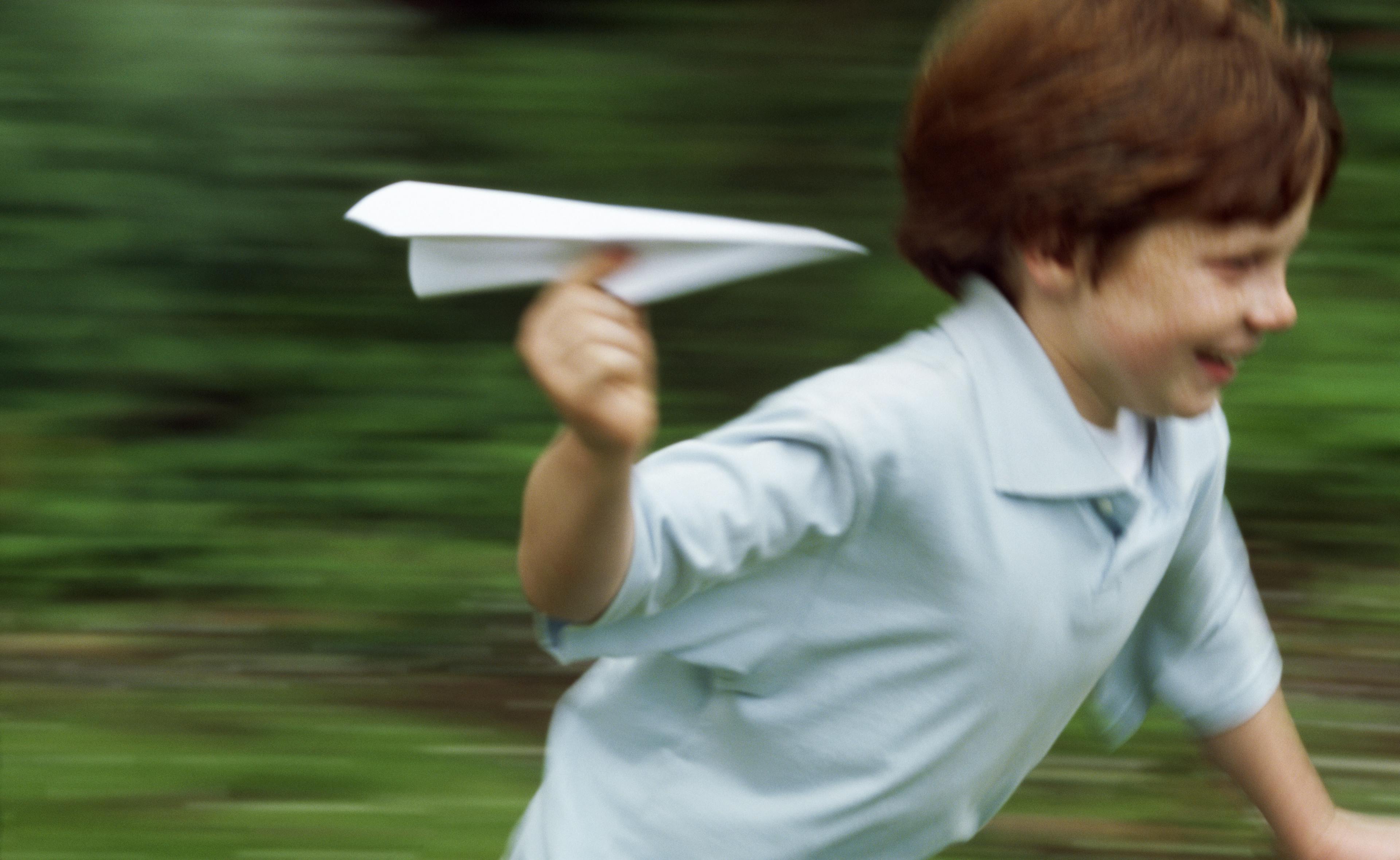 Ein Junge rennt mit Papierflieger in der Hand.