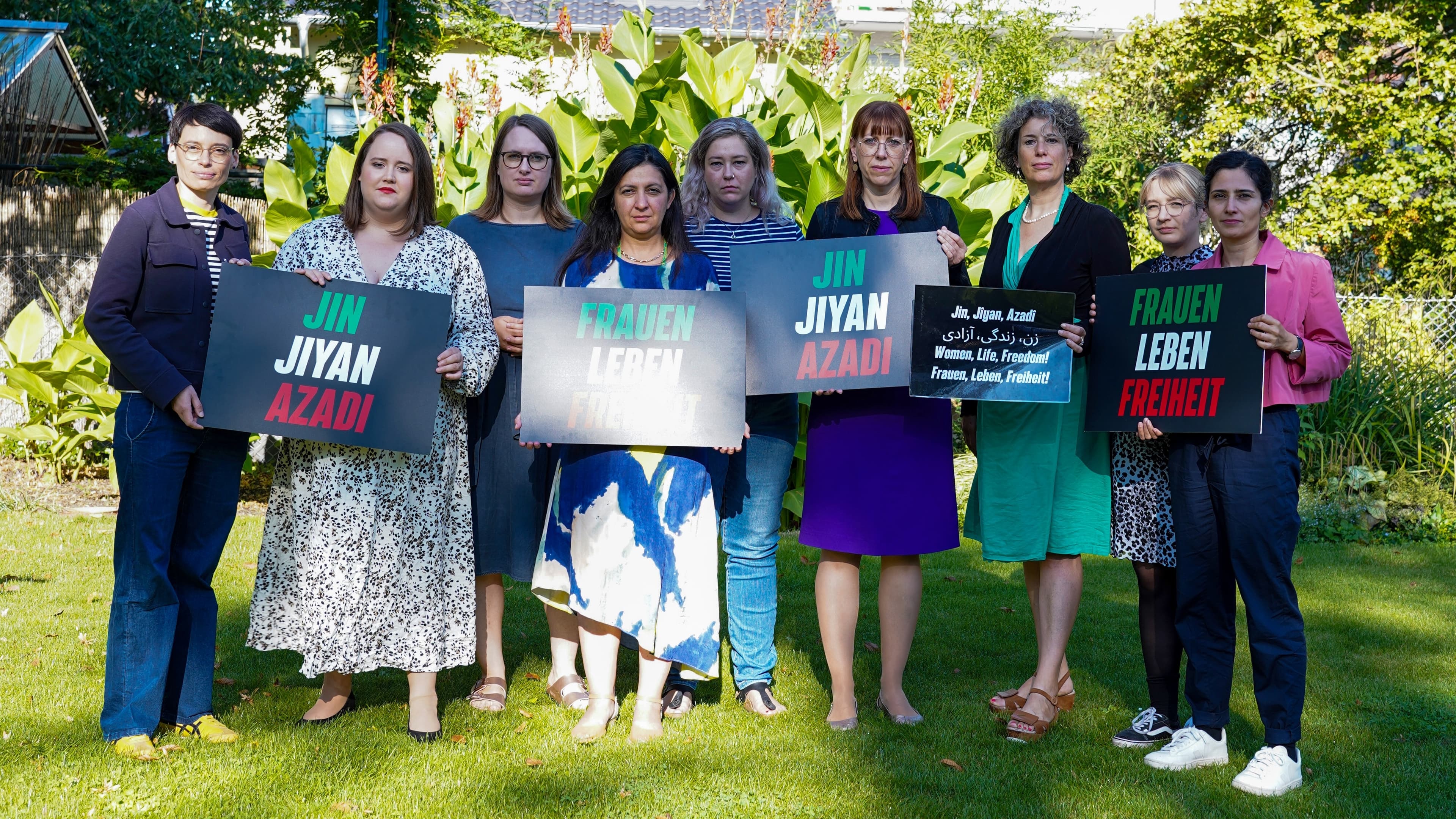 Eine Gruppe Frauen steht auf einem Rasen und hält Schilder.