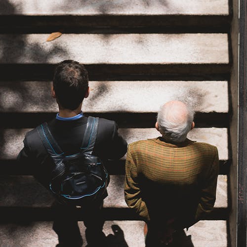 Ein junger und ein alter Mensch steigen nebeneinander eine Treppe empor.
