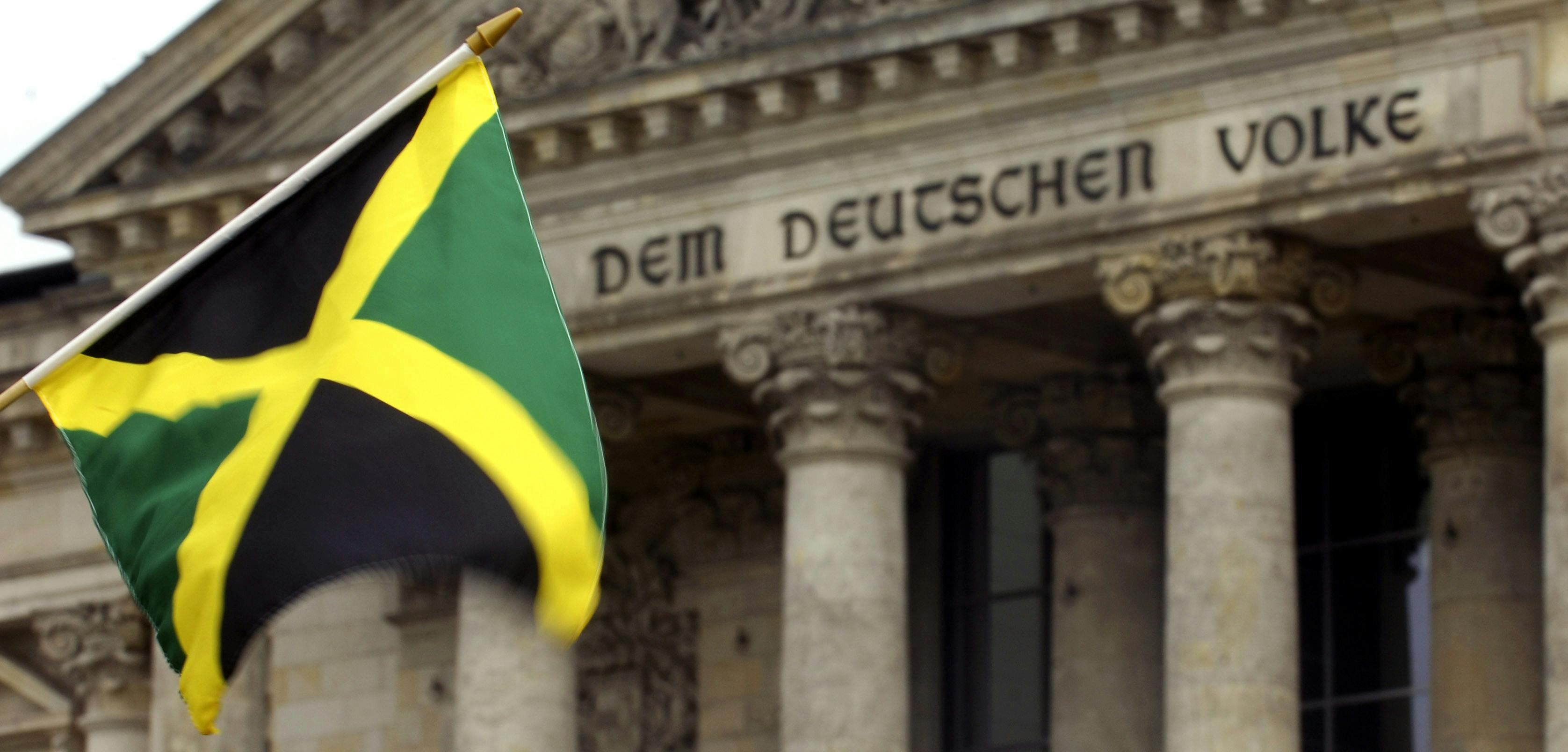 Eine Jamaika-Flagge wird vor das Reichstagsgebäude in Berlin gehalten. Auf dem Gebäude ist der Schriftzug "Dem deutschen Volke" zu sehen.
