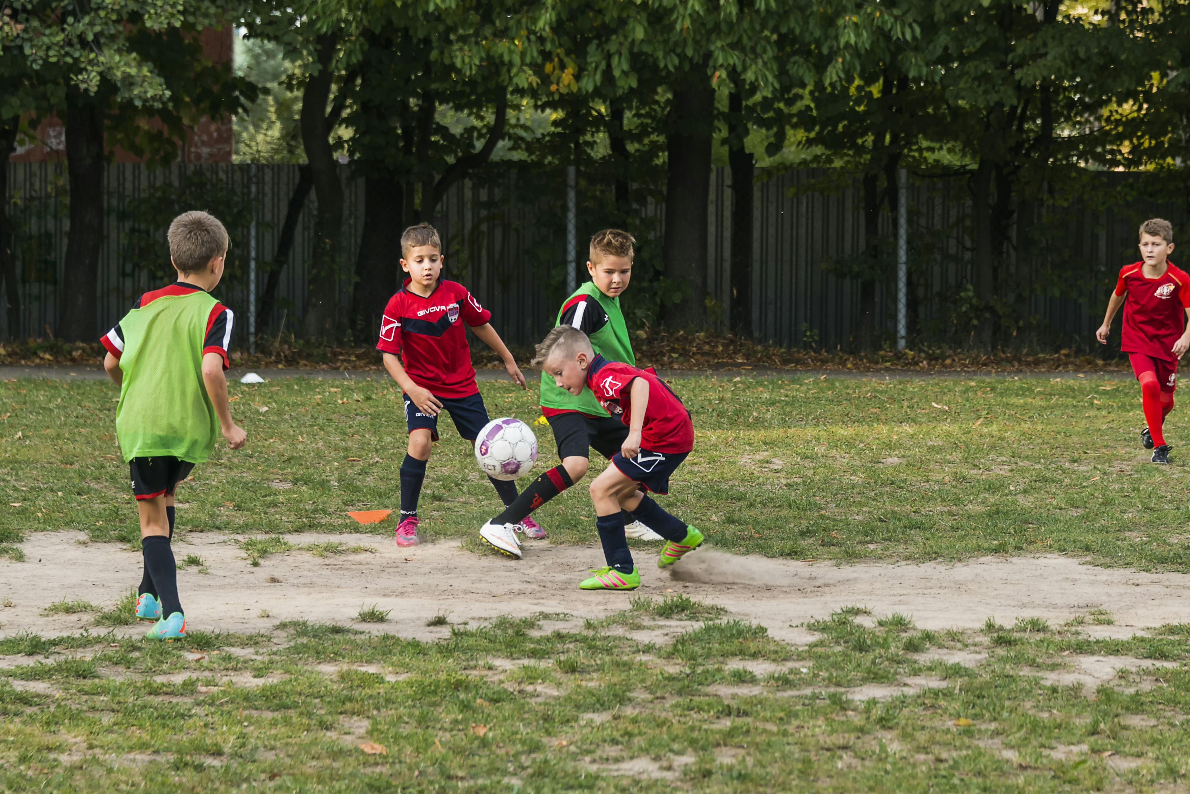 Kleine Kids spielen Fußball auf einem Bolzplatz. Sie tragen Fußballtrikots und Laibchen. Einer erkämpft sich den Ball und bereitet gerade einen Angriff vor.