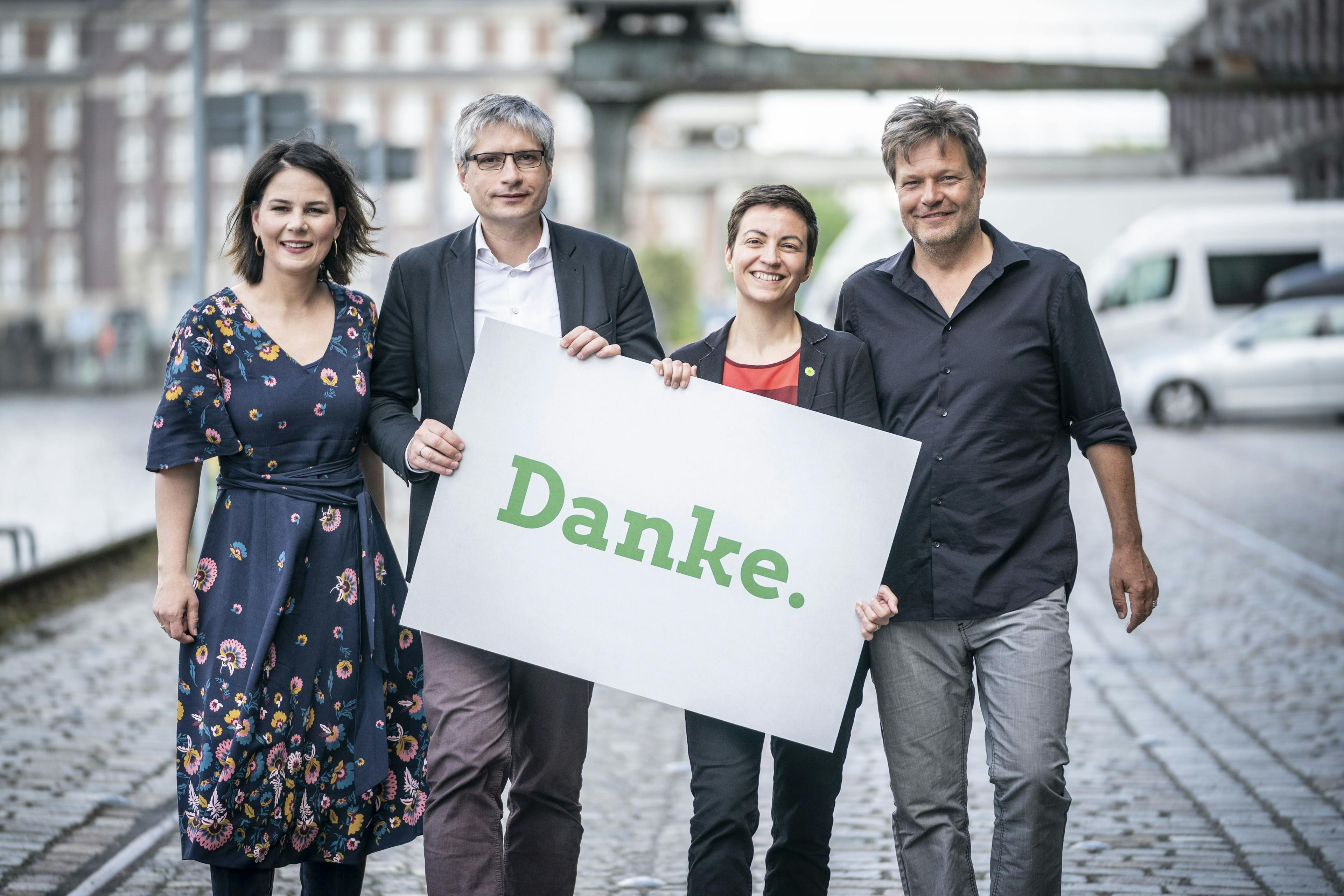 Annalena Baerbock, Sven Giegold, Ska Keller und Robert Habeck stehen nebeneinander und halten ein Schild mit der Aufschrift "Danke" in der Hand. Im Hintergrund ist eine Hafenpromenade zu sehen.