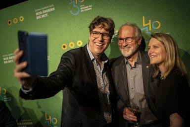 Michael Kellner macht mit Lukas Beckmann und Marianne Birthler ein Selfie vor einer grünen Fotowand.