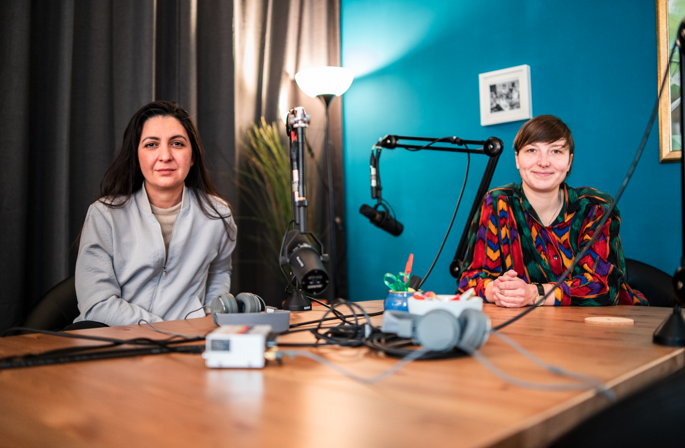 Pegah Edalatian und Hanna Forys sitzen an einem Tisch, auf dem ein Mikro steht. Im hintergrund eine blaue Wand und eine Lampe.