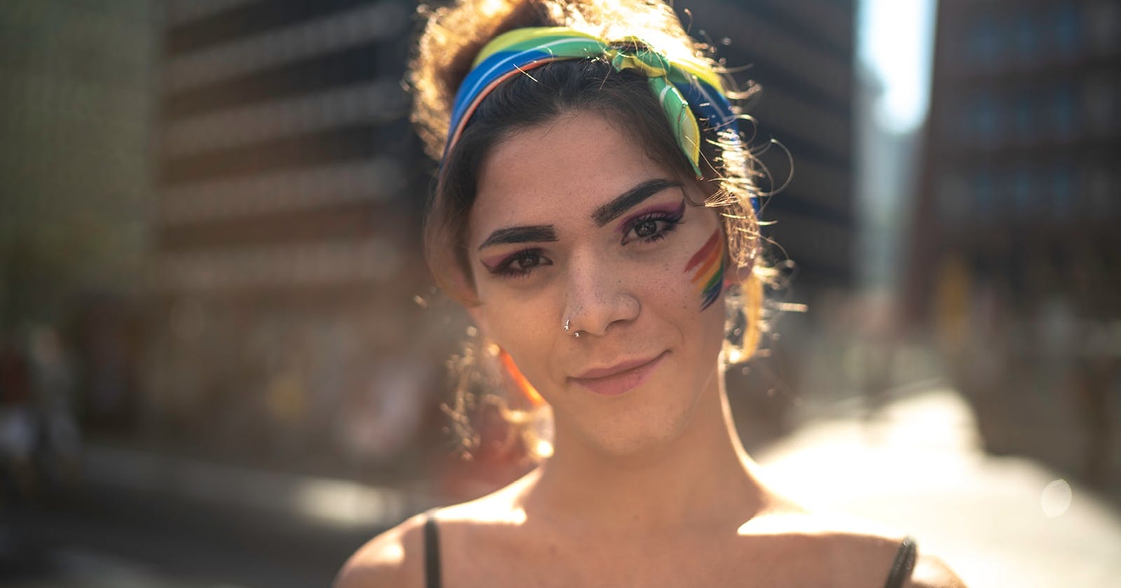 Portrait einer  jungen Frau mit Pride-Flagge auf der Wange und buntem Tuch in den Haaren