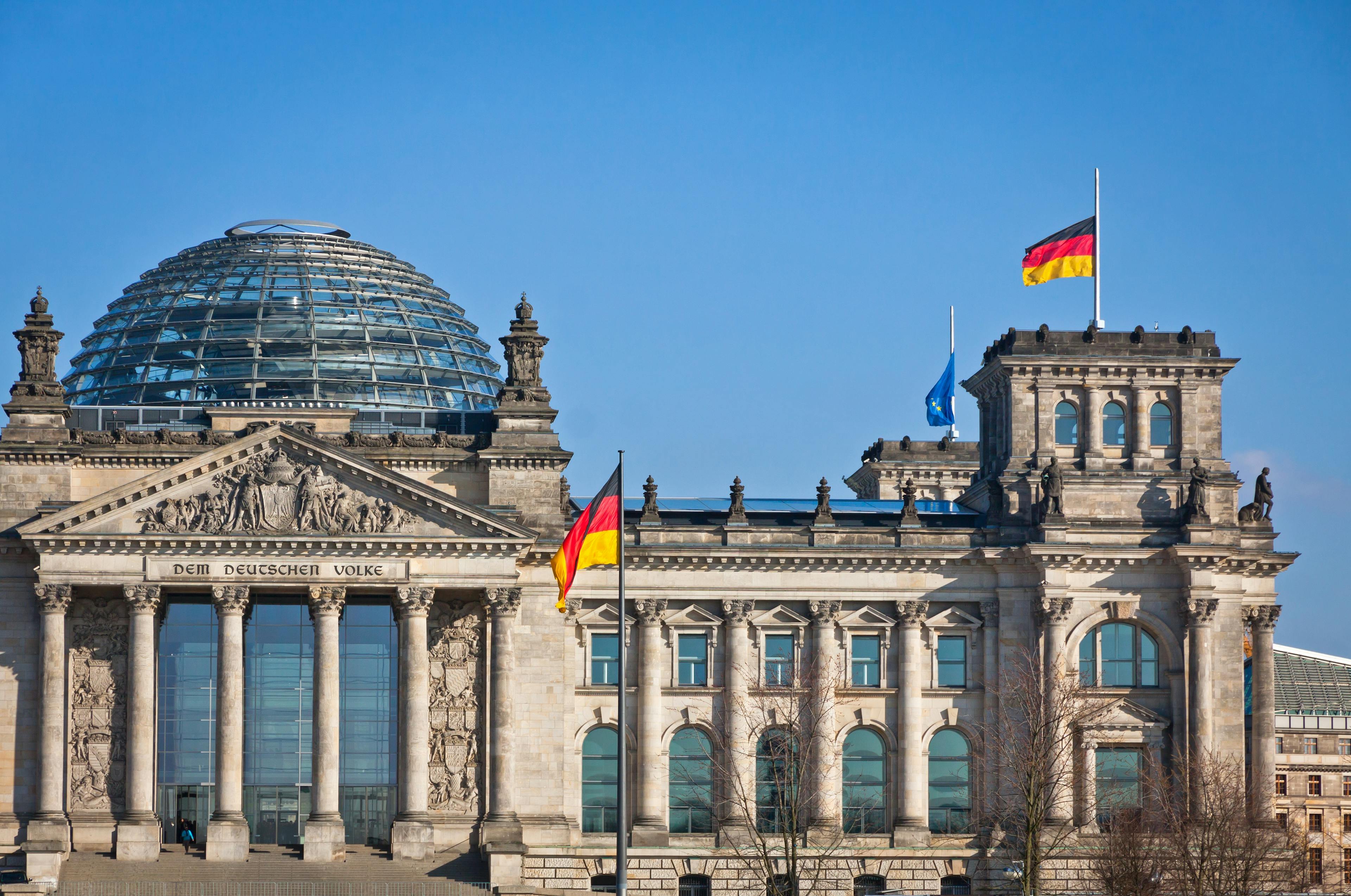 Reichstagsgebäude mit gehisster Flagge vor blauem Himmel.