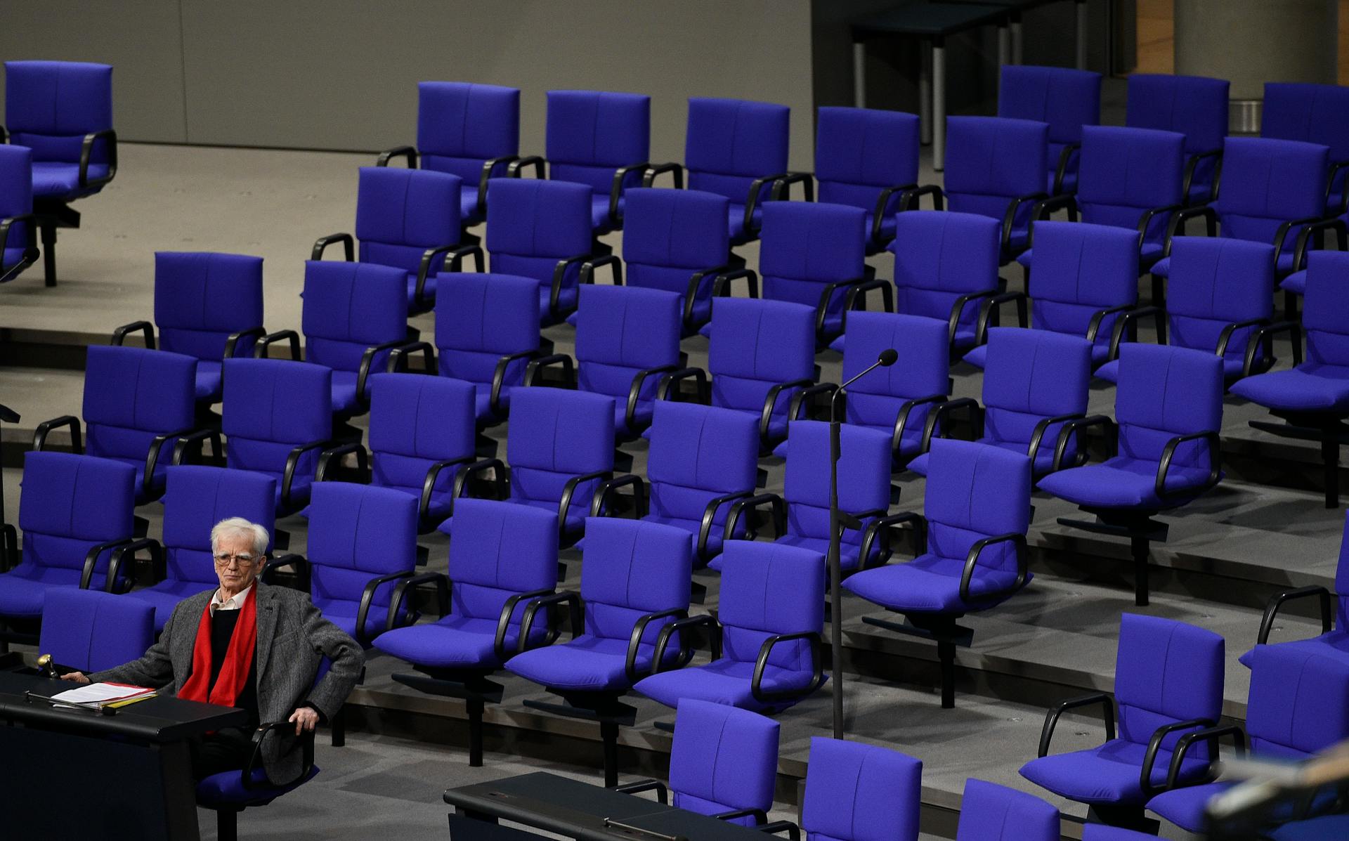 Hans-Christian Ströbele sitzt miet rotem Schal alleine im Plenum des Bundestags